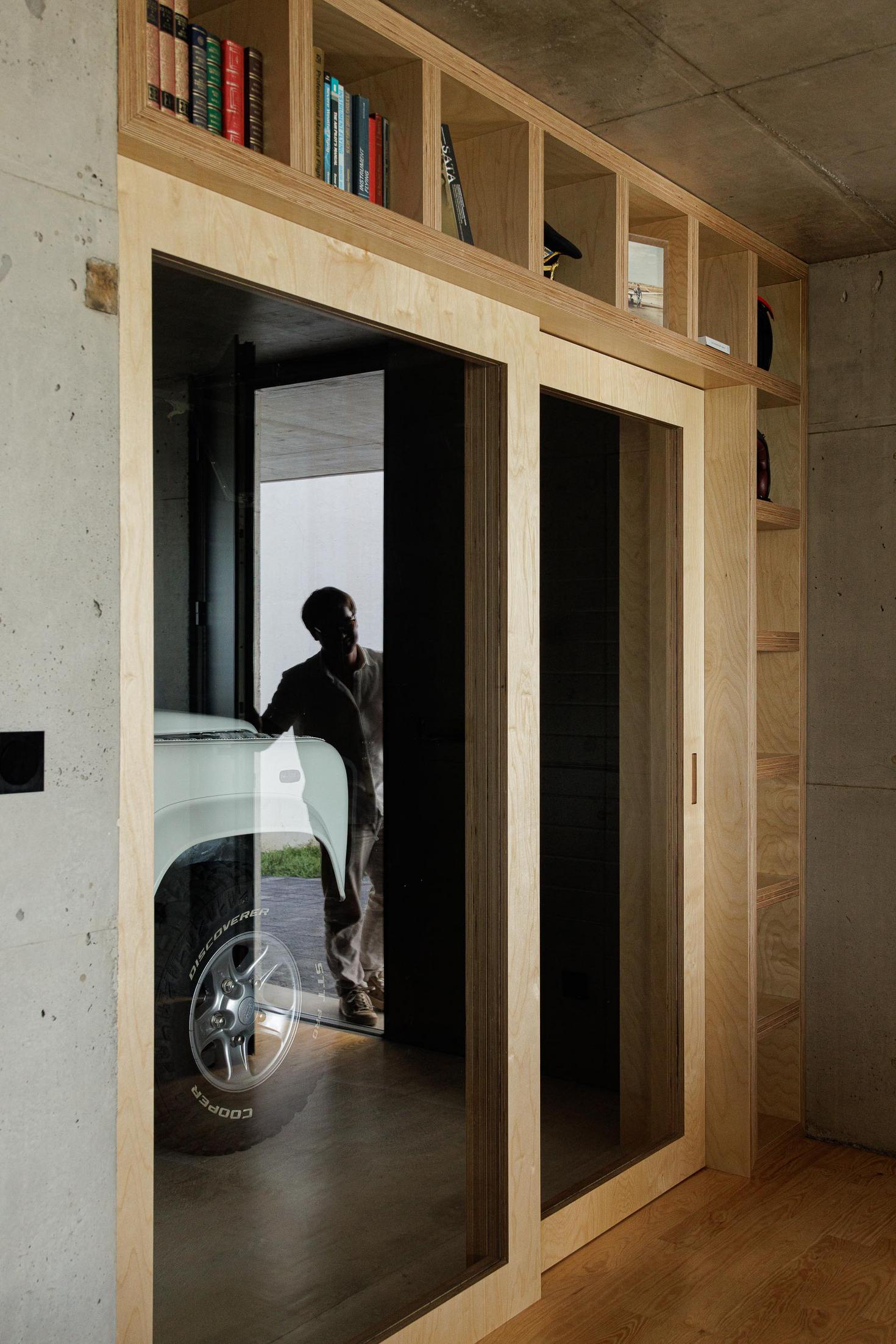 Garagem: Porta deslizante em madeira com prateleiras. Carro branco estacionado no interior. — Casa da Rocha Quebrada arquitetura SO Arquitetura & Design em São Miguel