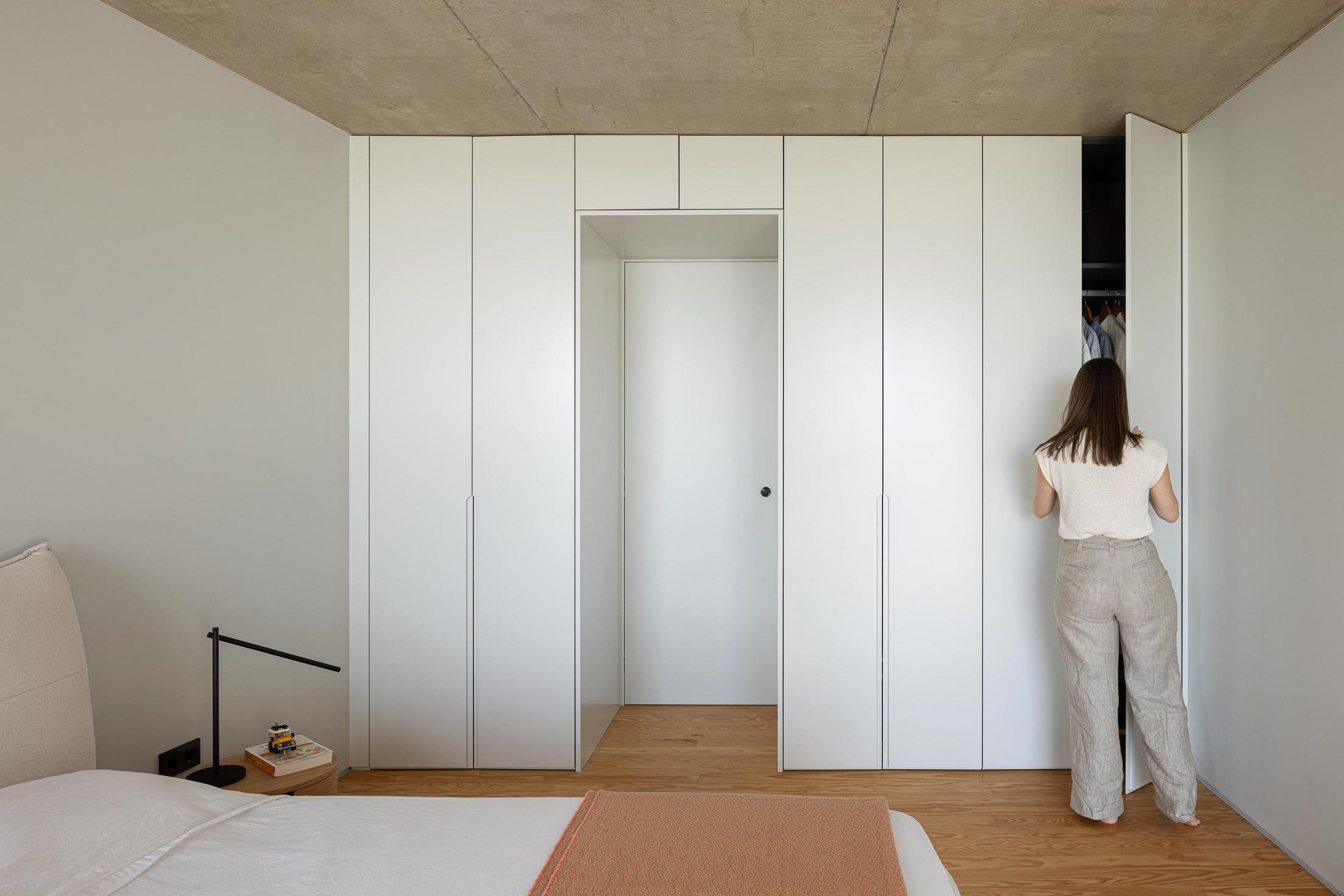 Quarto: Roupeiro branco embutido. Pavimento em madeira e cama com roupa de cama clara. — Casa da Rocha Quebrada arquitetura SO Arquitetura & Design em São Miguel