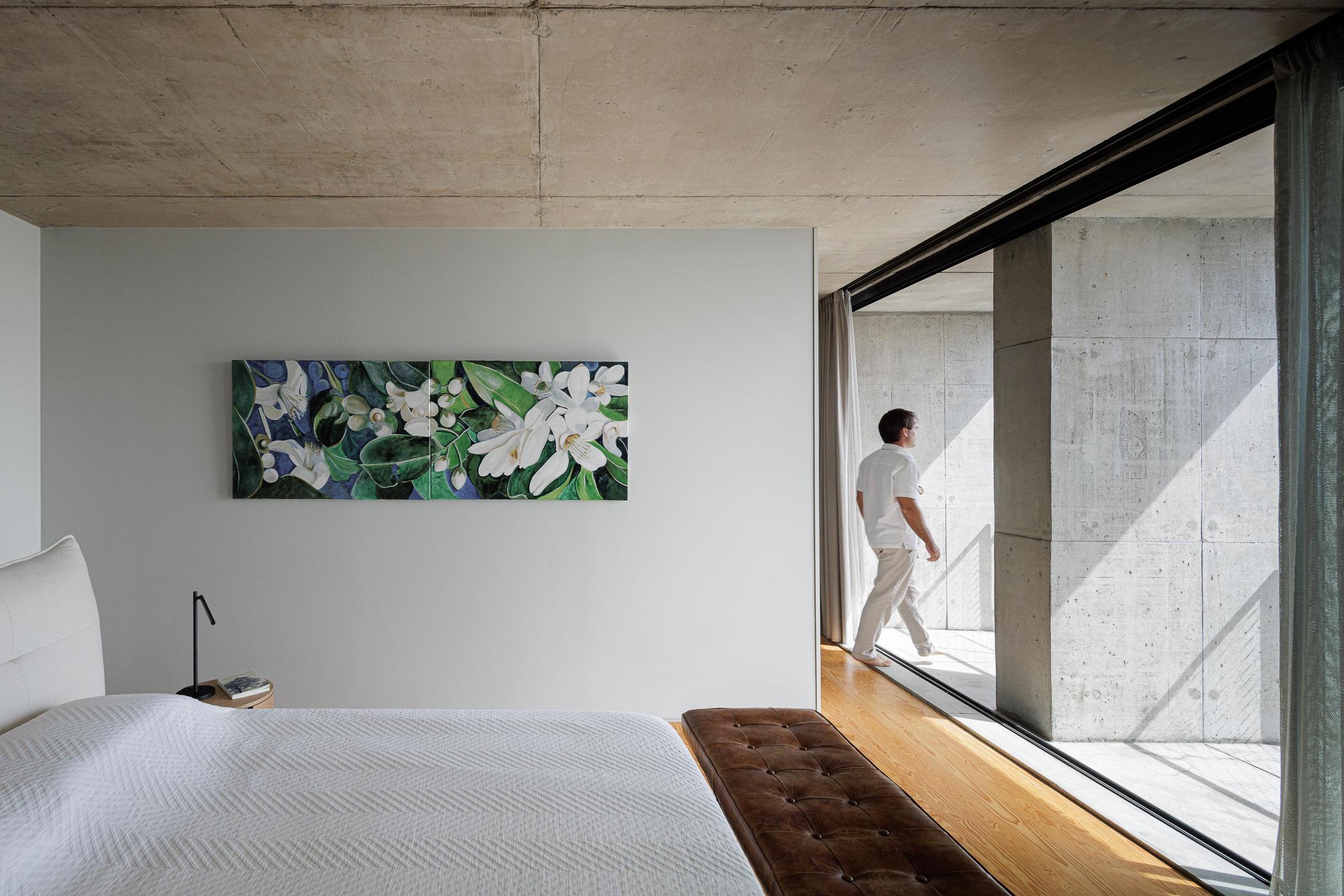Quarto: Cama branca e varanda com vista para o mar. Pavimento em madeira e cortinas claras. — Casa da Rocha Quebrada arquitetura SO Arquitetura & Design em São Miguel