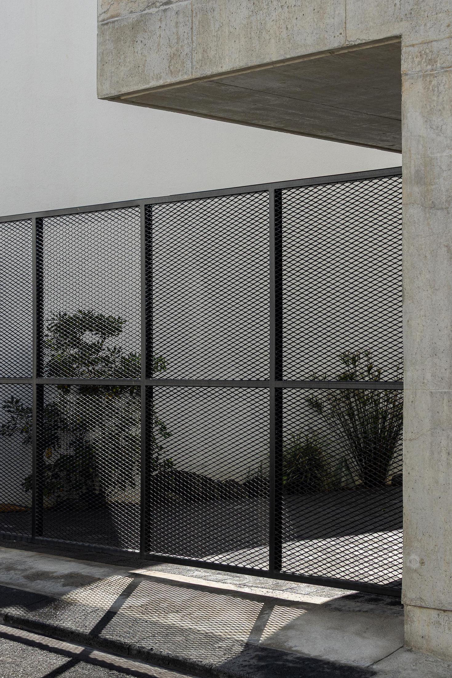 Exterior: Detalhe do portão metálico e fachada em betão. Sombra projetada no pavimento. — Casa da Rocha Quebrada arquitetura SO Arquitetura & Design em São Miguel