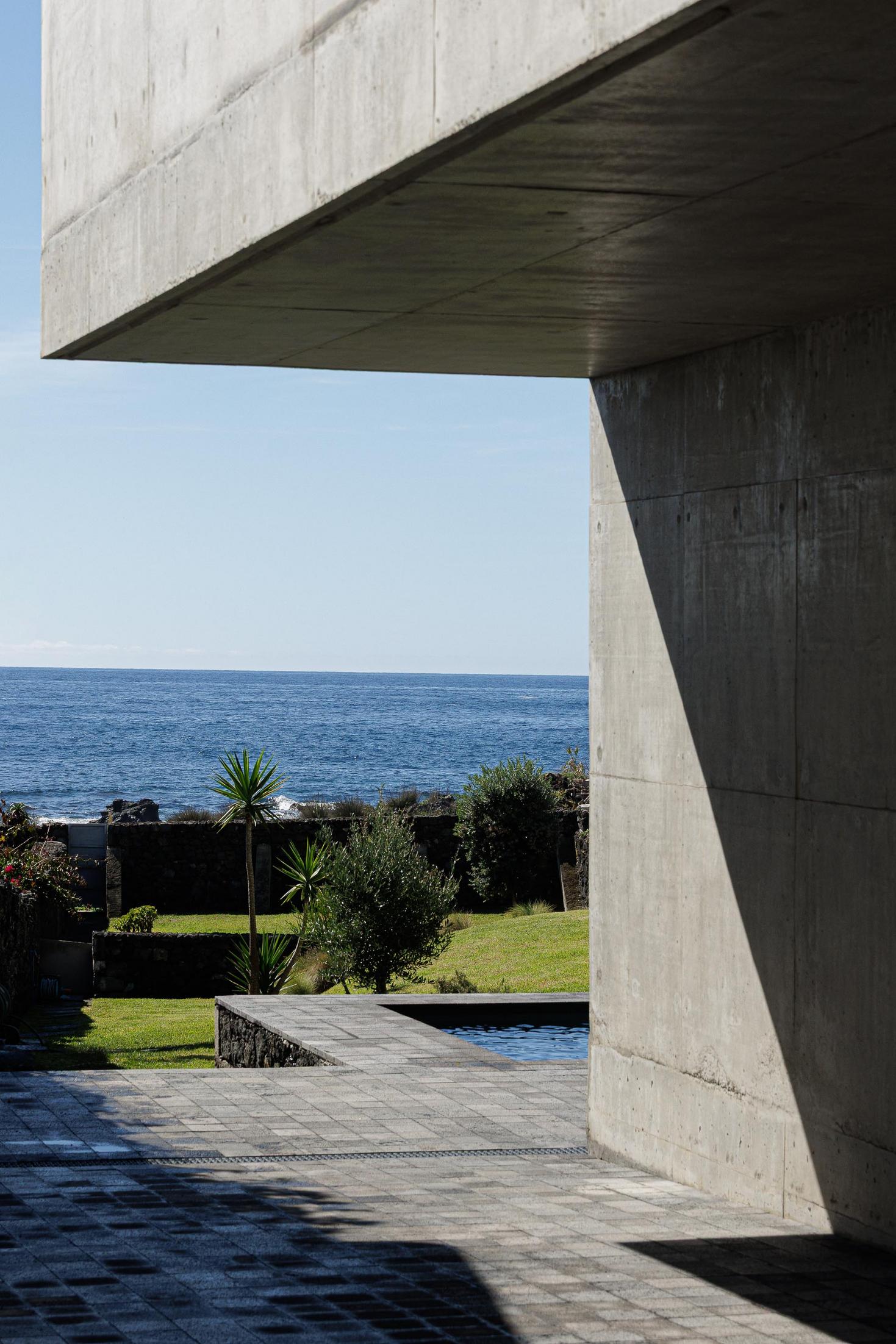 Exterior: Vista para o mar através da estrutura em betão. Pavimento em pedra e relvado. — Casa da Rocha Quebrada arquitetura SO Arquitetura & Design em São Miguel
