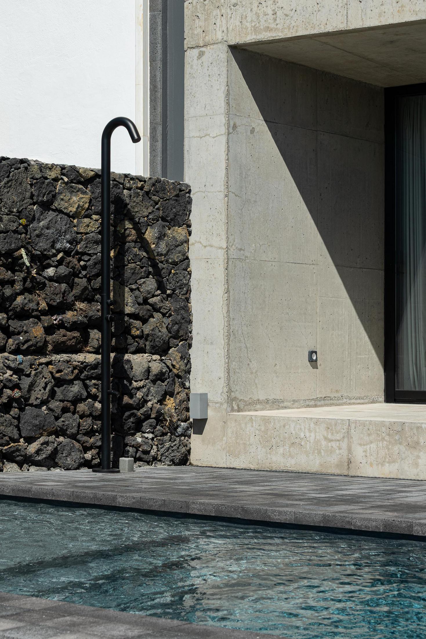 Exterior: Duche preto junto à piscina com parede de pedra vulcânica e betão. — Casa da Rocha Quebrada arquitetura SO Arquitetura & Design em São Miguel