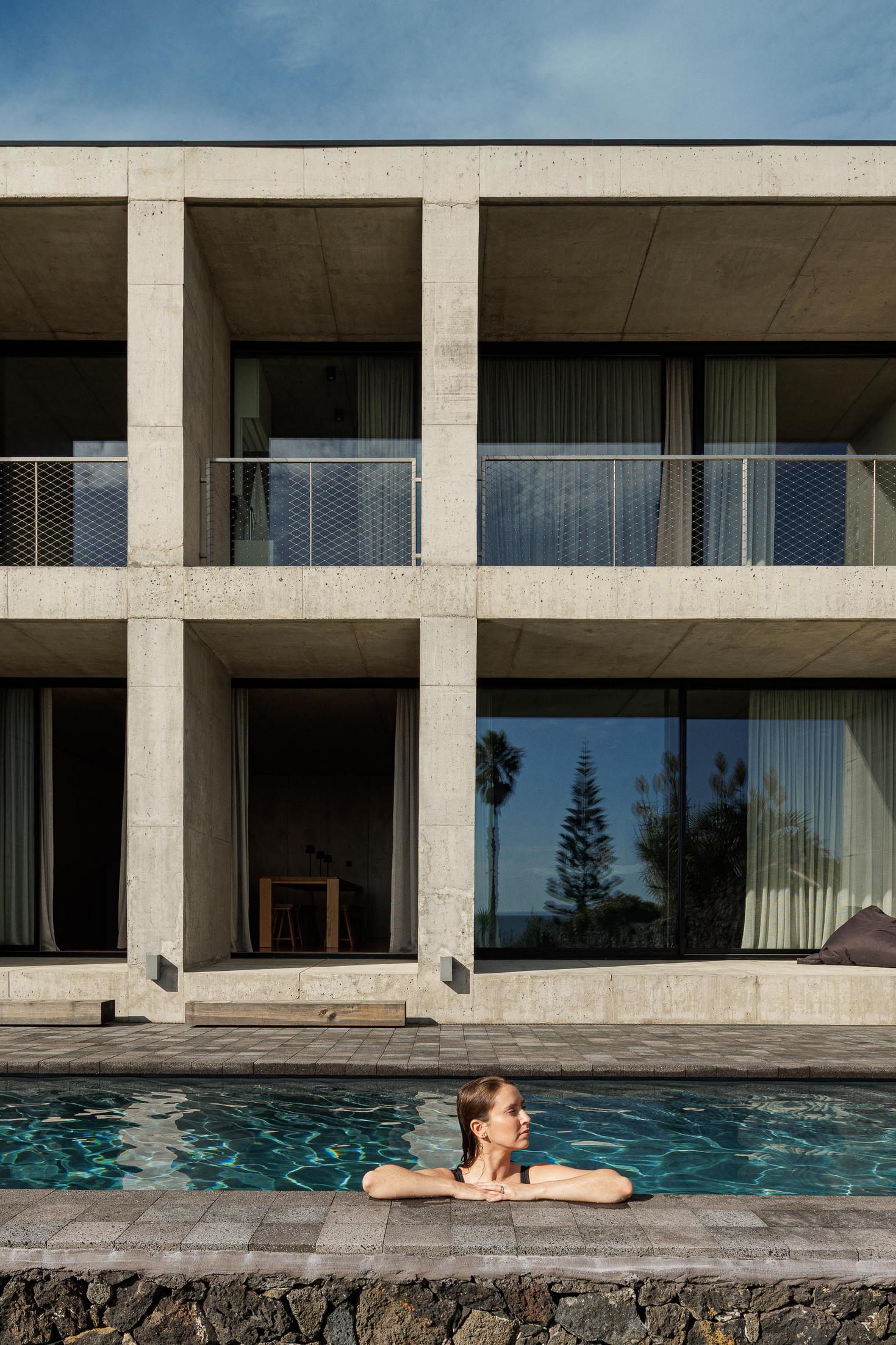 Exterior: Mulher na piscina com vista para o edifício em betão. Reflexos na água. — Casa da Rocha Quebrada arquitetura SO Arquitetura & Design em São Miguel