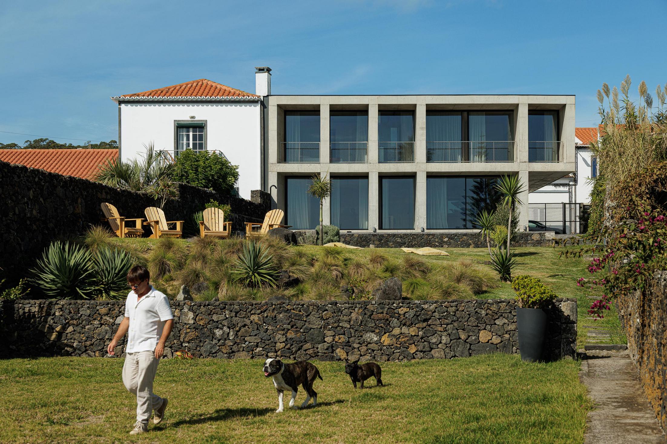 Exterior: Edifício em betão com jardim e piscina. Crianças e cães no relvado. — Casa da Rocha Quebrada arquitetura SO Arquitetura & Design em São Miguel