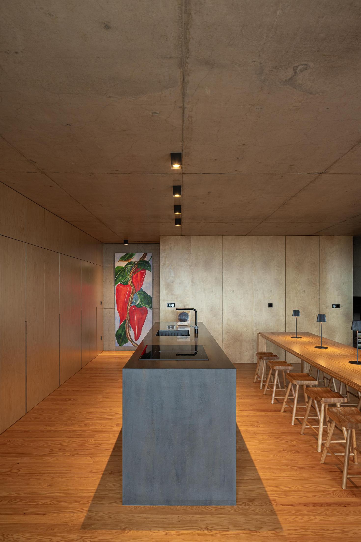 Cozinha: Ilha central em betão e mesa de jantar em madeira. Pavimento em madeira. — Casa da Rocha Quebrada arquitetura SO Arquitetura & Design em São Miguel