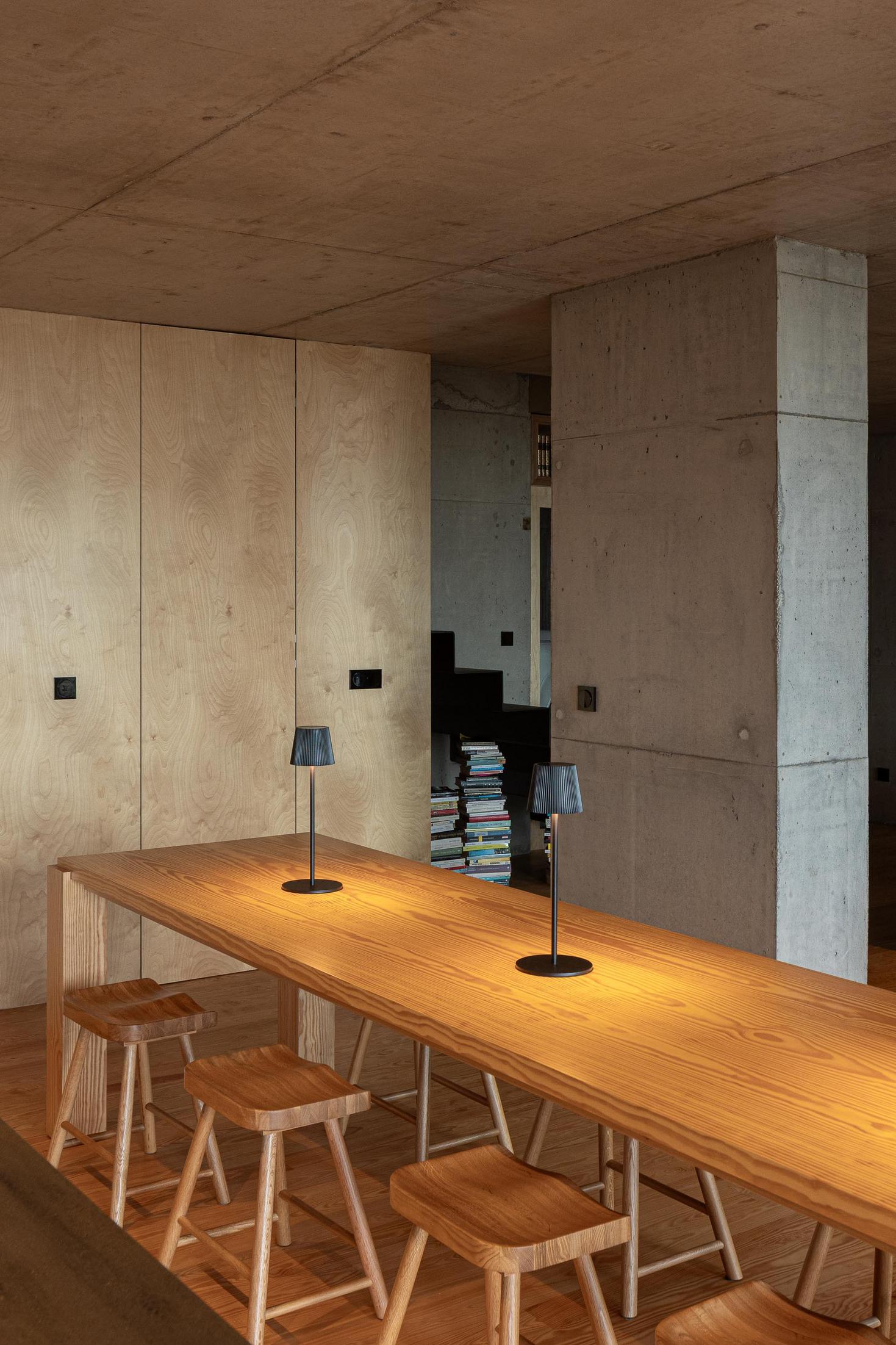Sala de jantar: Mesa de madeira com bancos e candeeiro. Escadas e parede em betão. — Casa da Rocha Quebrada arquitetura SO Arquitetura & Design em São Miguel