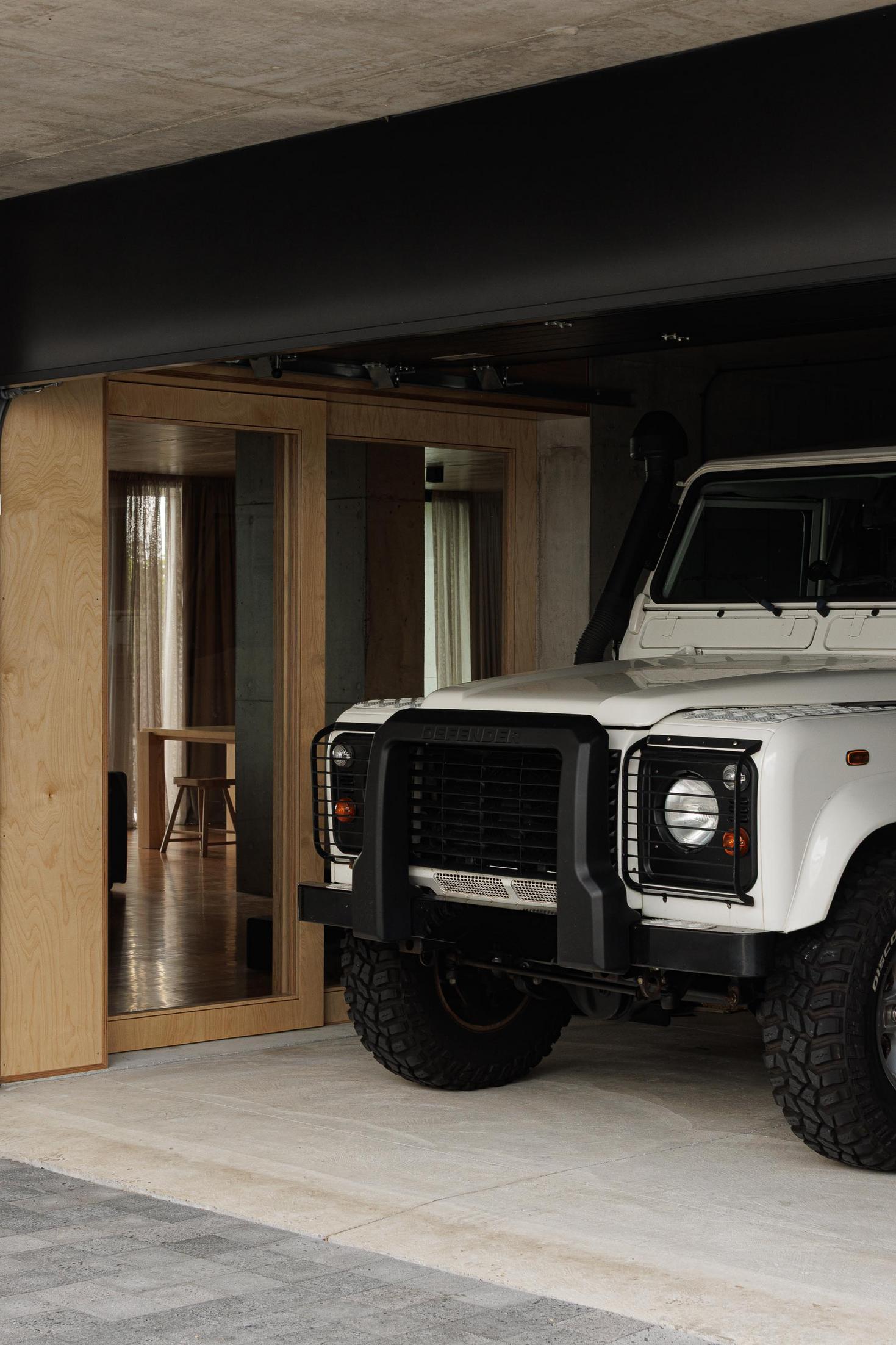 Garagem: Carro branco estacionado. Porta deslizante em madeira e iluminação interior. — Casa da Rocha Quebrada arquitetura SO Arquitetura & Design em São Miguel