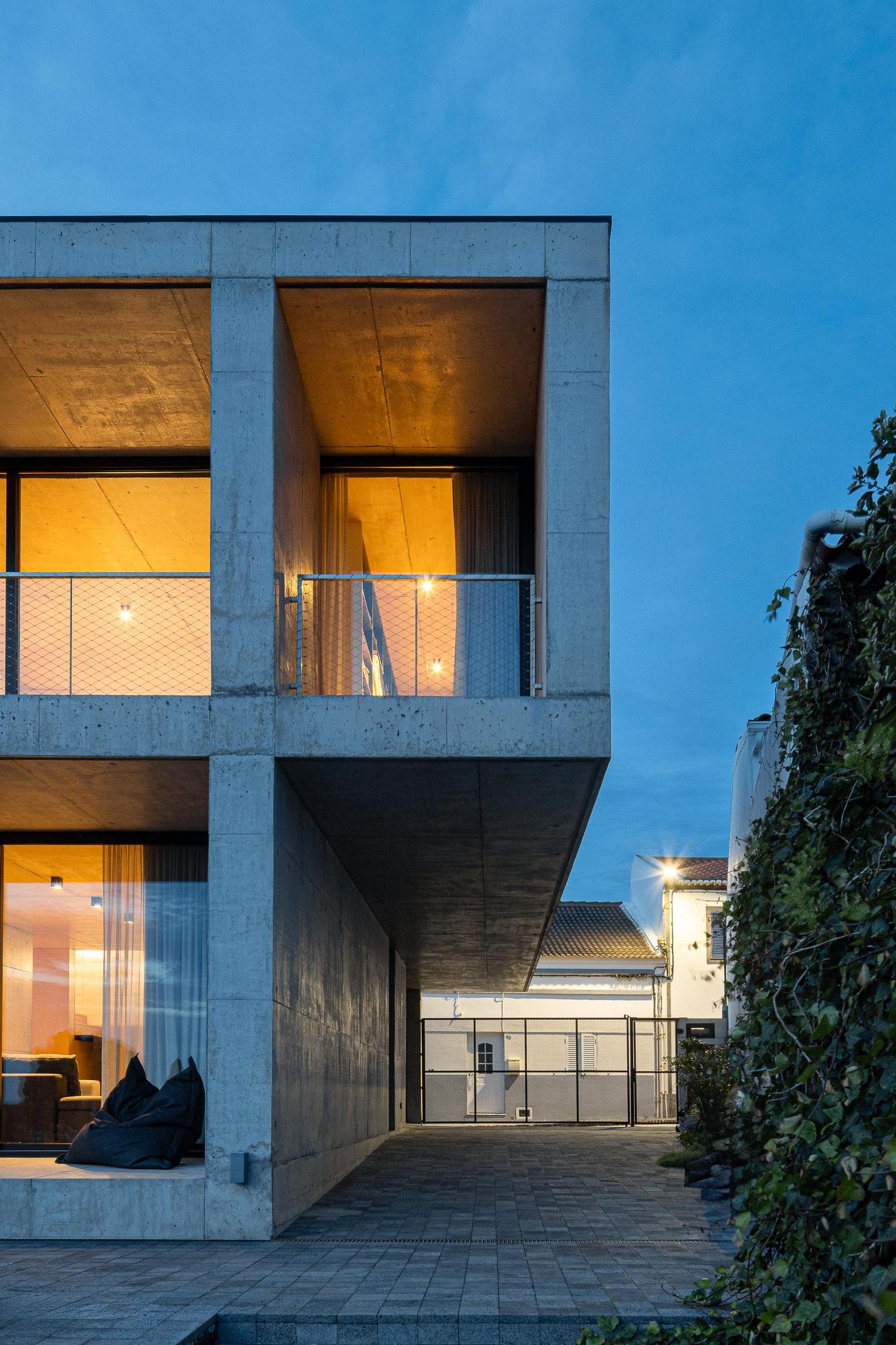 Exterior: Vista lateral do edifício em betão. Vegetação exuberante e portão metálico. — Casa da Rocha Quebrada arquitetura SO Arquitetura & Design em São Miguel