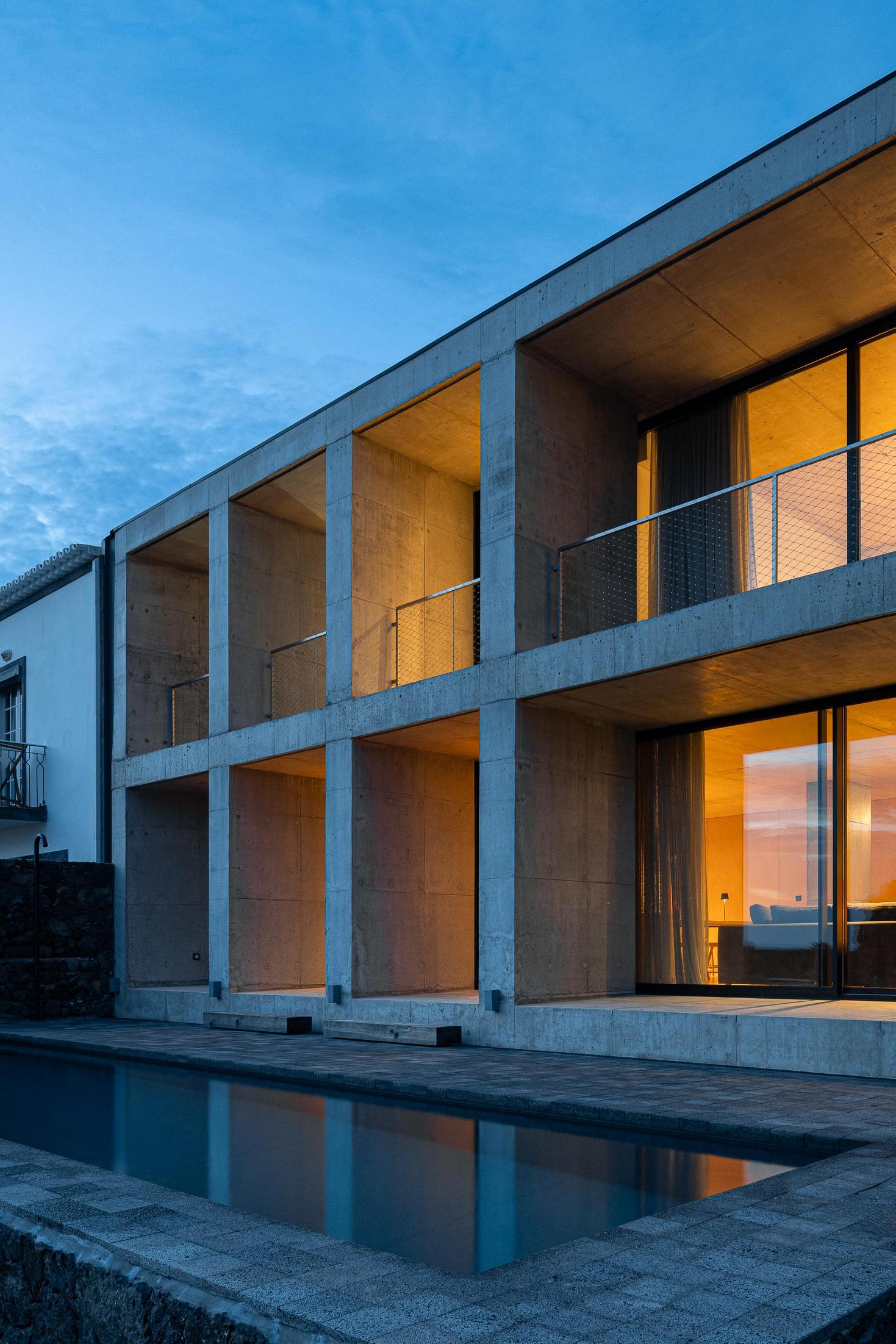Fachada: Edifício moderno em betão com varandas e piscina. Arquitetura minimalista com reflexos no céu azul. — Casa da Rocha Quebrada arquitetura SO Arquitetura & Design em São Miguel