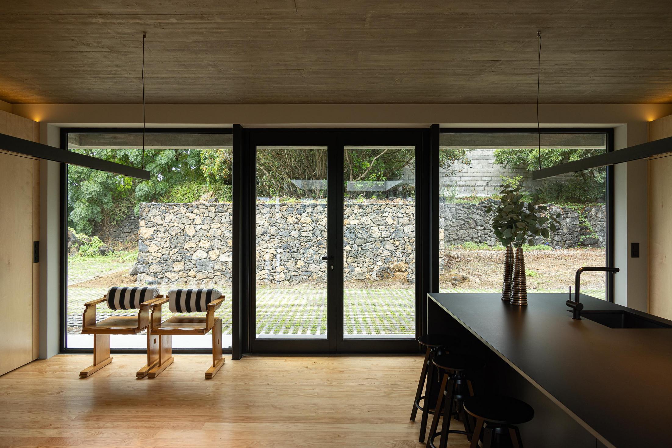 Cozinha: Ilha central preta, armários em contraplacado e pavimento em madeira. Cadeiras de madeira com padrão listrado. — Casa CR arquitetura SO Arquitetura & Design em São Miguel