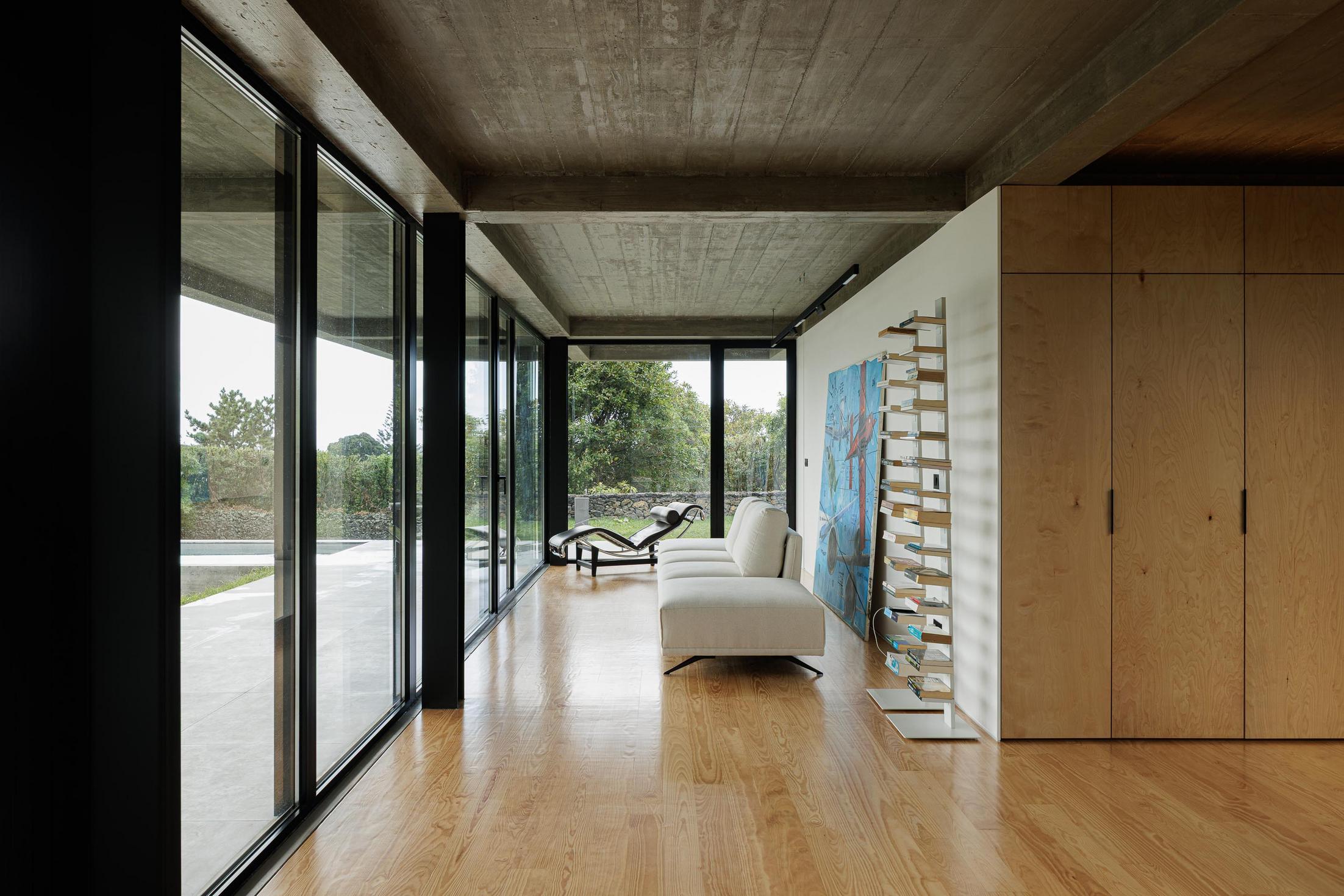 Sala de estar: Sofá branco, chaise longue e estante com livros. Grandes janelas com vista para o exterior. — Casa CR arquitetura SO Arquitetura & Design em São Miguel