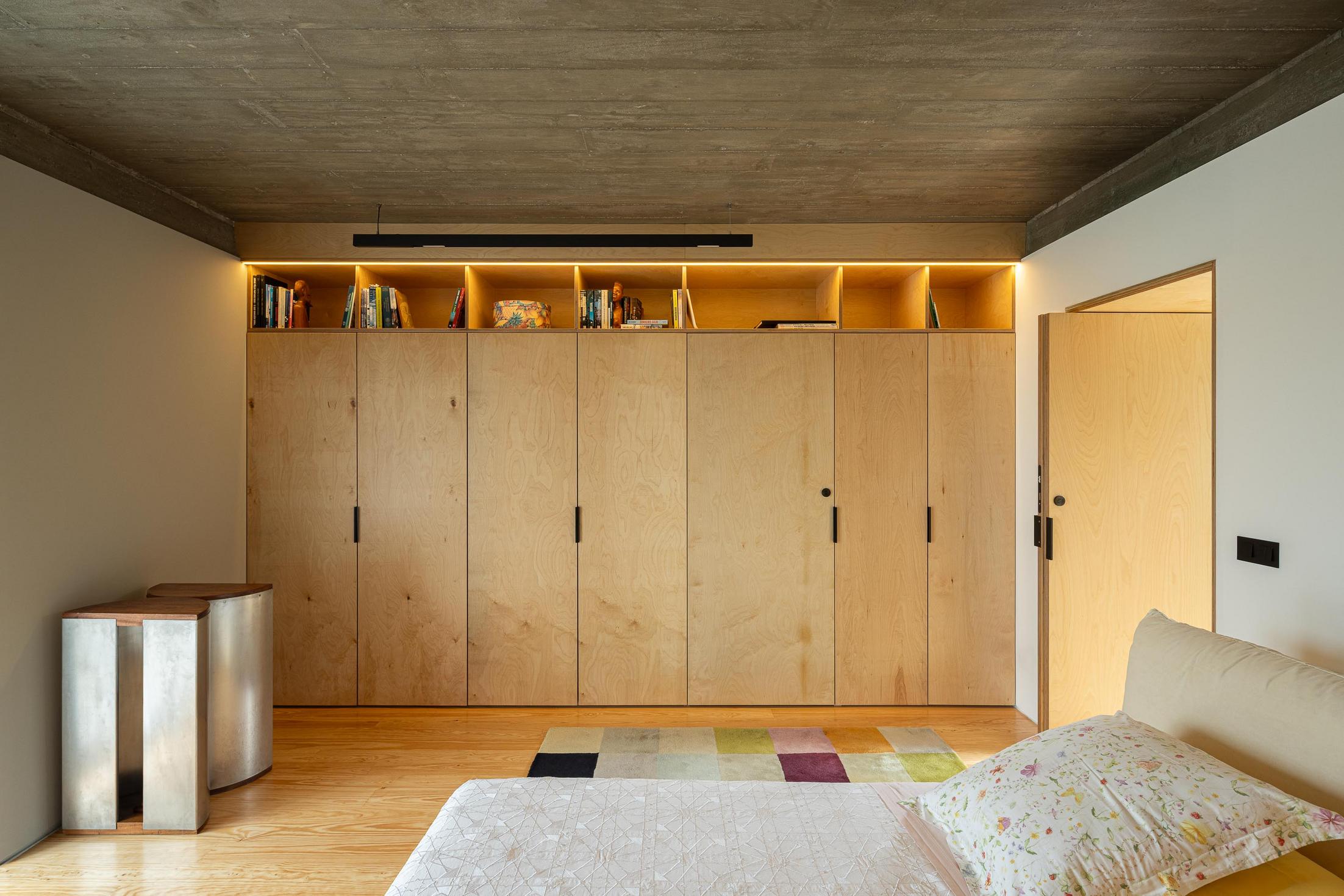 Quarto: Roupeiro em contraplacado com prateleiras, pavimento em madeira e alcatifa geométrica. — Casa CR arquitetura SO Arquitetura & Design em São Miguel