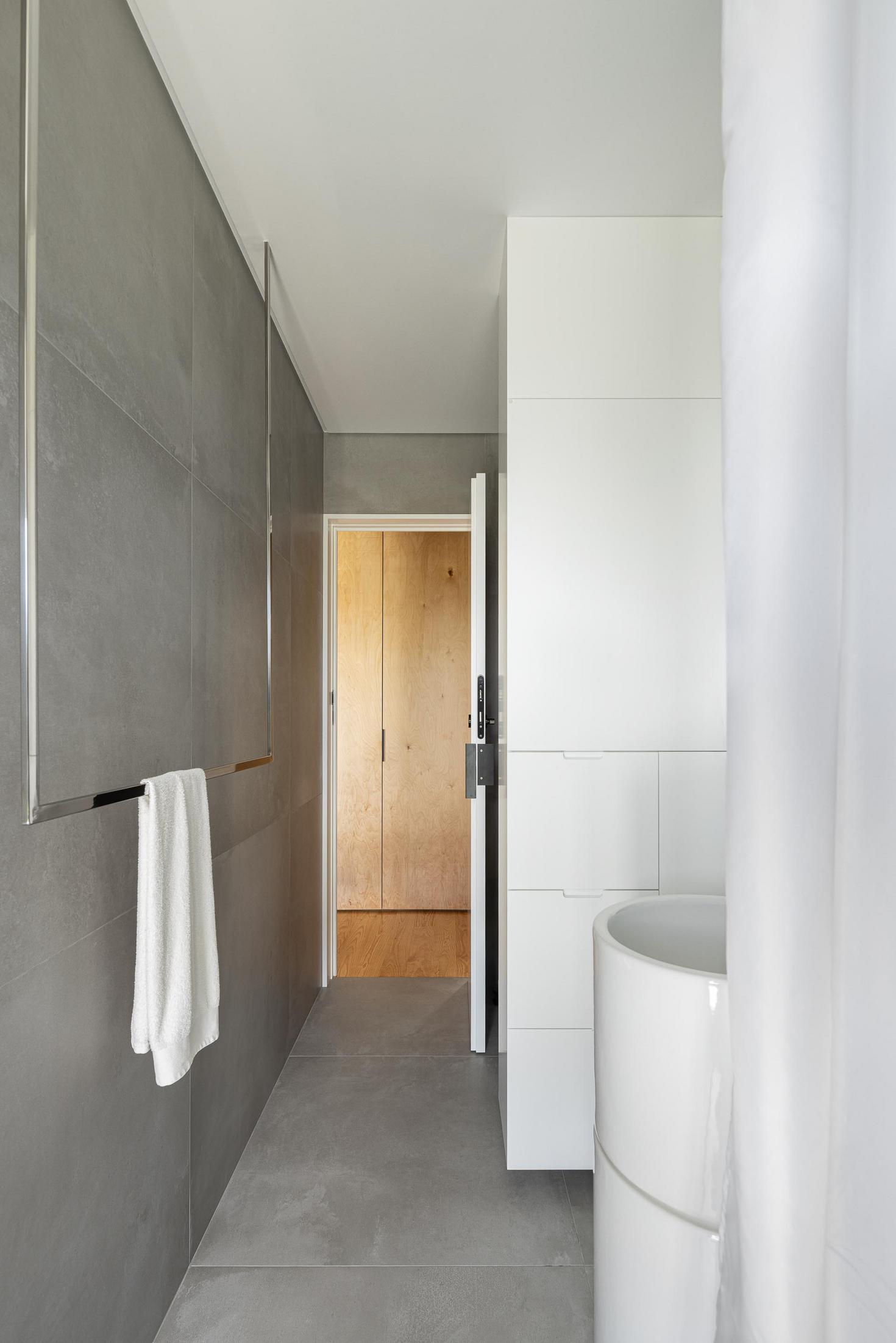 Casa de banho: Banheira branca, revestimento cerâmico cinza e roupeiro branco. — Casa CR arquitetura SO Arquitetura & Design em São Miguel