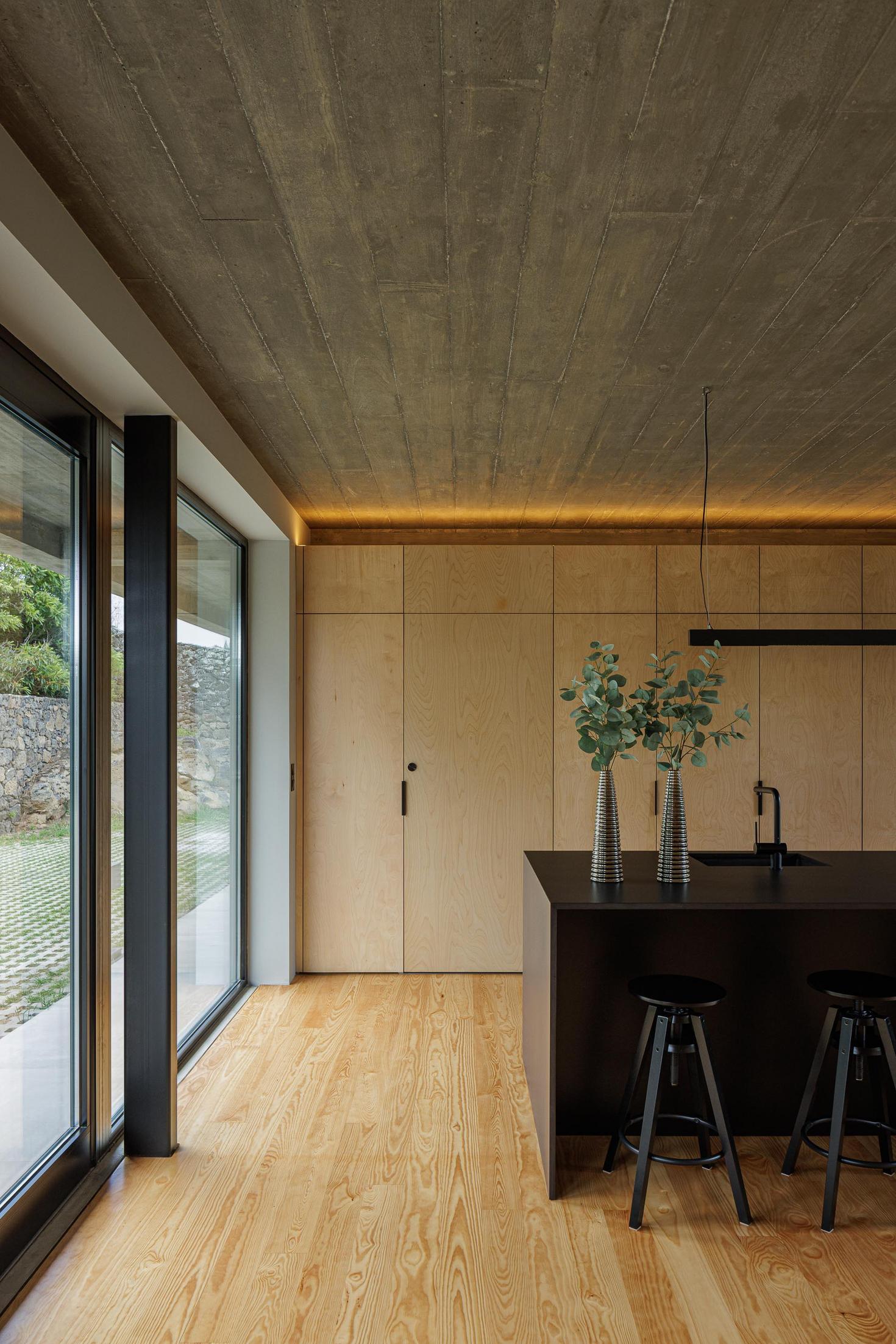 Cozinha: Ilha central preta, armários em contraplacado e pavimento em madeira clara. — Casa CR arquitetura SO Arquitetura & Design em São Miguel