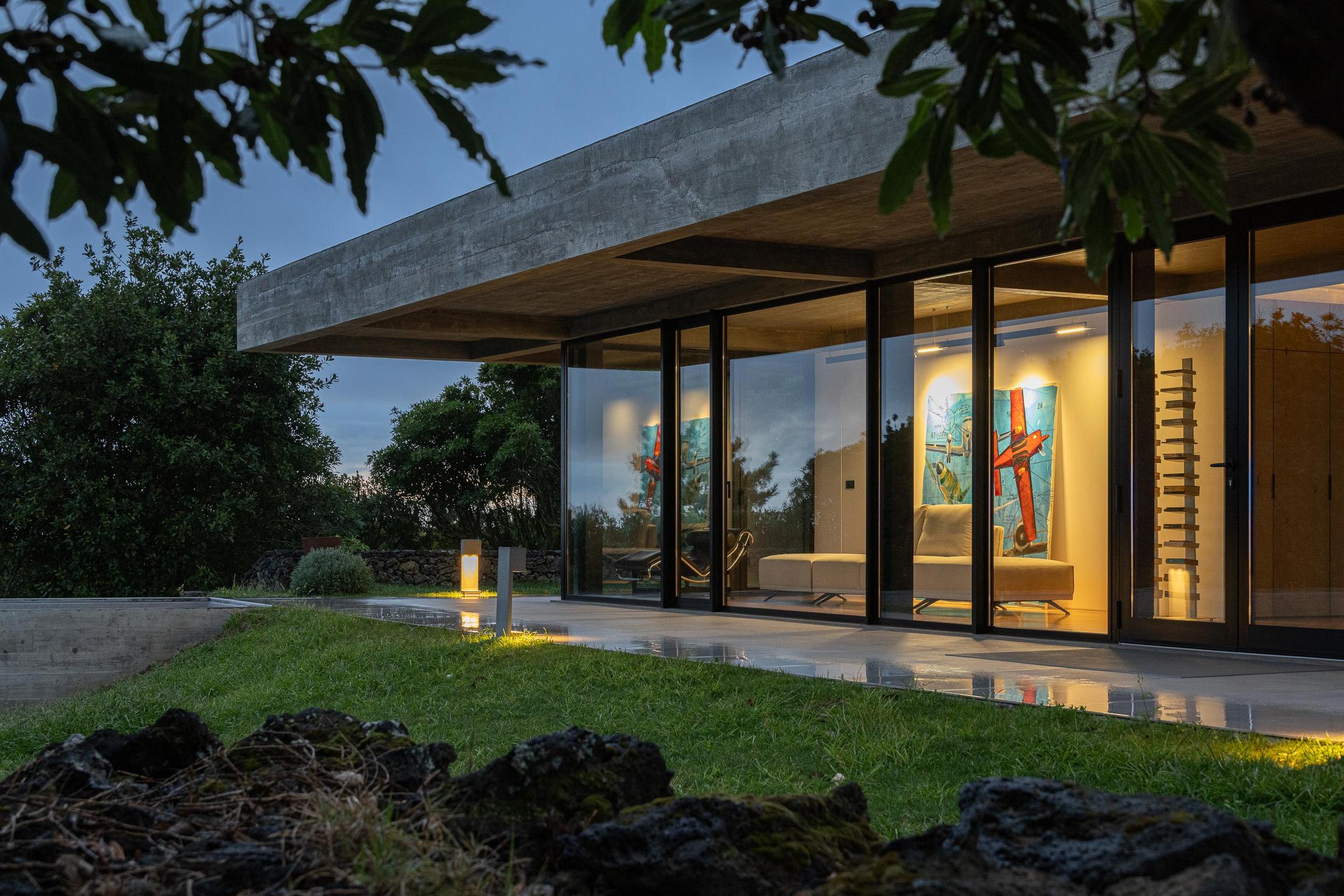 Exterior: Fachada da casa com iluminação noturna e relvado. — Casa CR arquitetura SO Arquitetura & Design em São Miguel