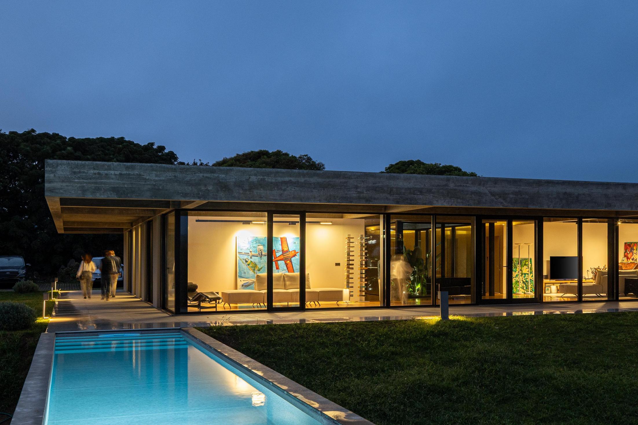 Exterior: Fachada da casa com iluminação noturna e piscina. — Casa CR arquitetura SO Arquitetura & Design em São Miguel