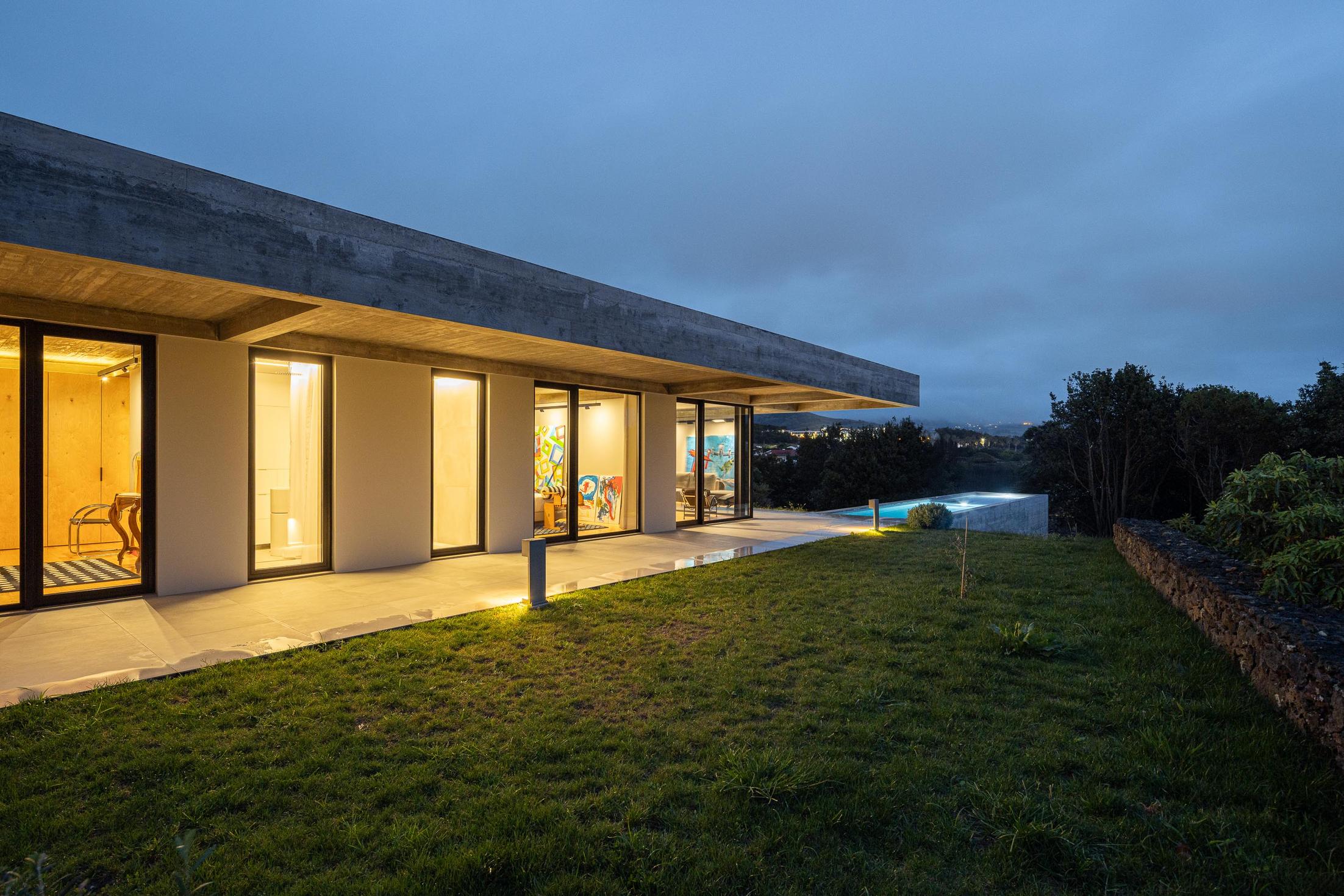 Exterior: Fachada da casa com iluminação noturna e relvado. — Casa CR arquitetura SO Arquitetura & Design em São Miguel