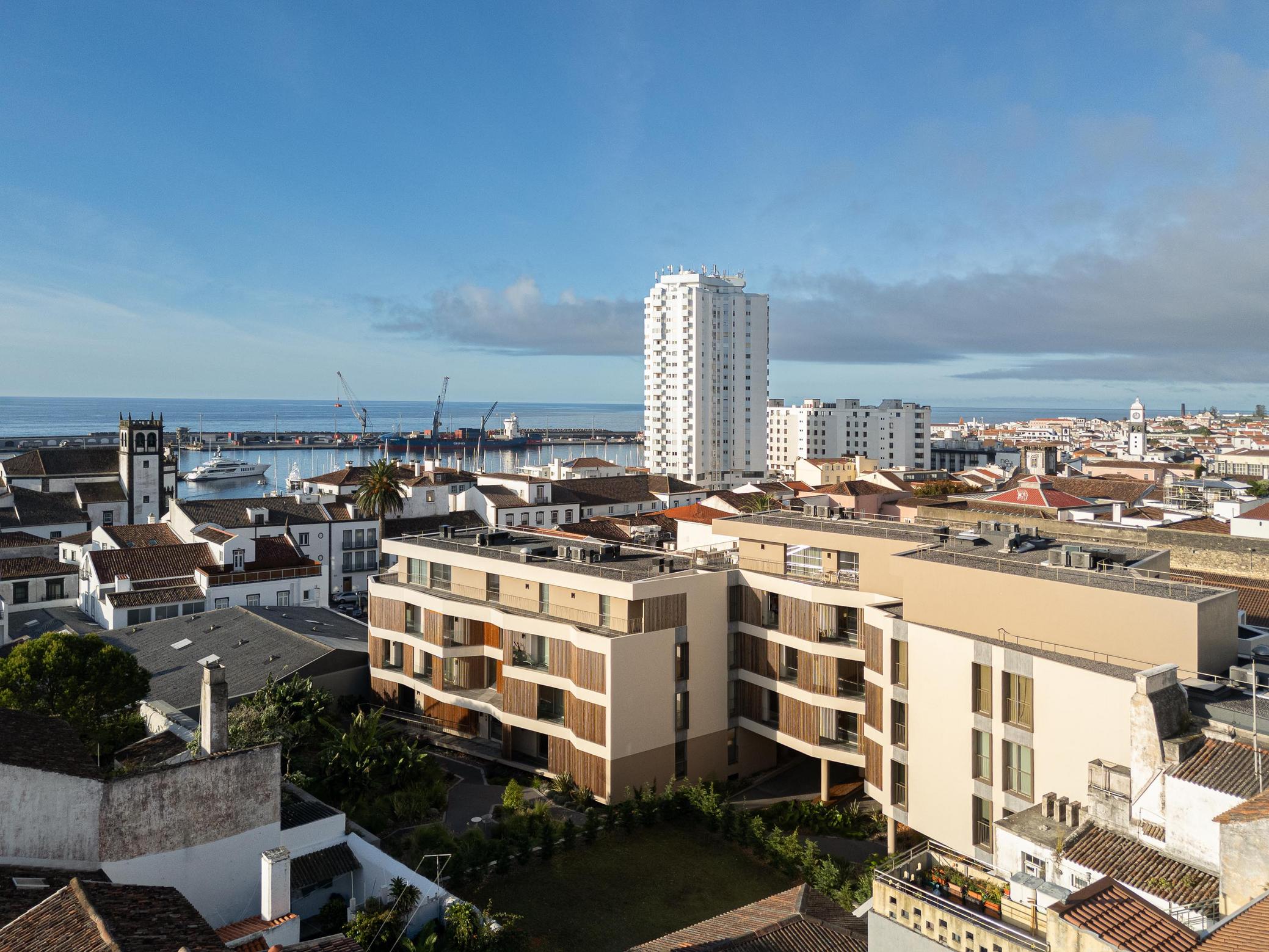 Vista da cidade: Condomínio moderno com detalhes em madeira, integrado na paisagem urbana de Ponta Delgada, com vista para o mar. — ERNESTO DO CANTO - condomínio arquitetura BOX arquitectos em Ponta Delgada
