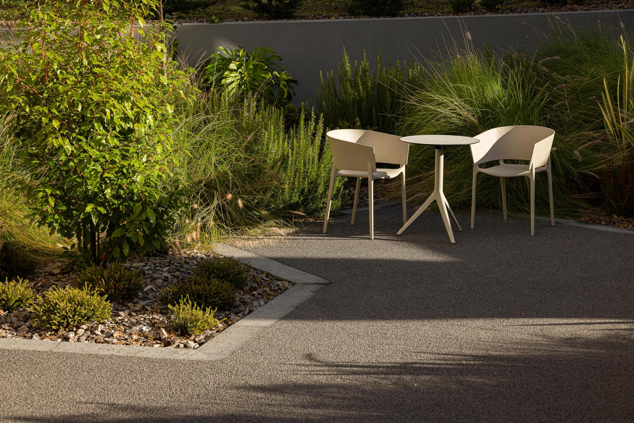 Jardim: Espaço exterior com mesa e cadeiras, pavimento em agregado e vegetação diversa. — ERNESTO DO CANTO - condomínio arquitetura BOX arquitectos em Ponta Delgada
