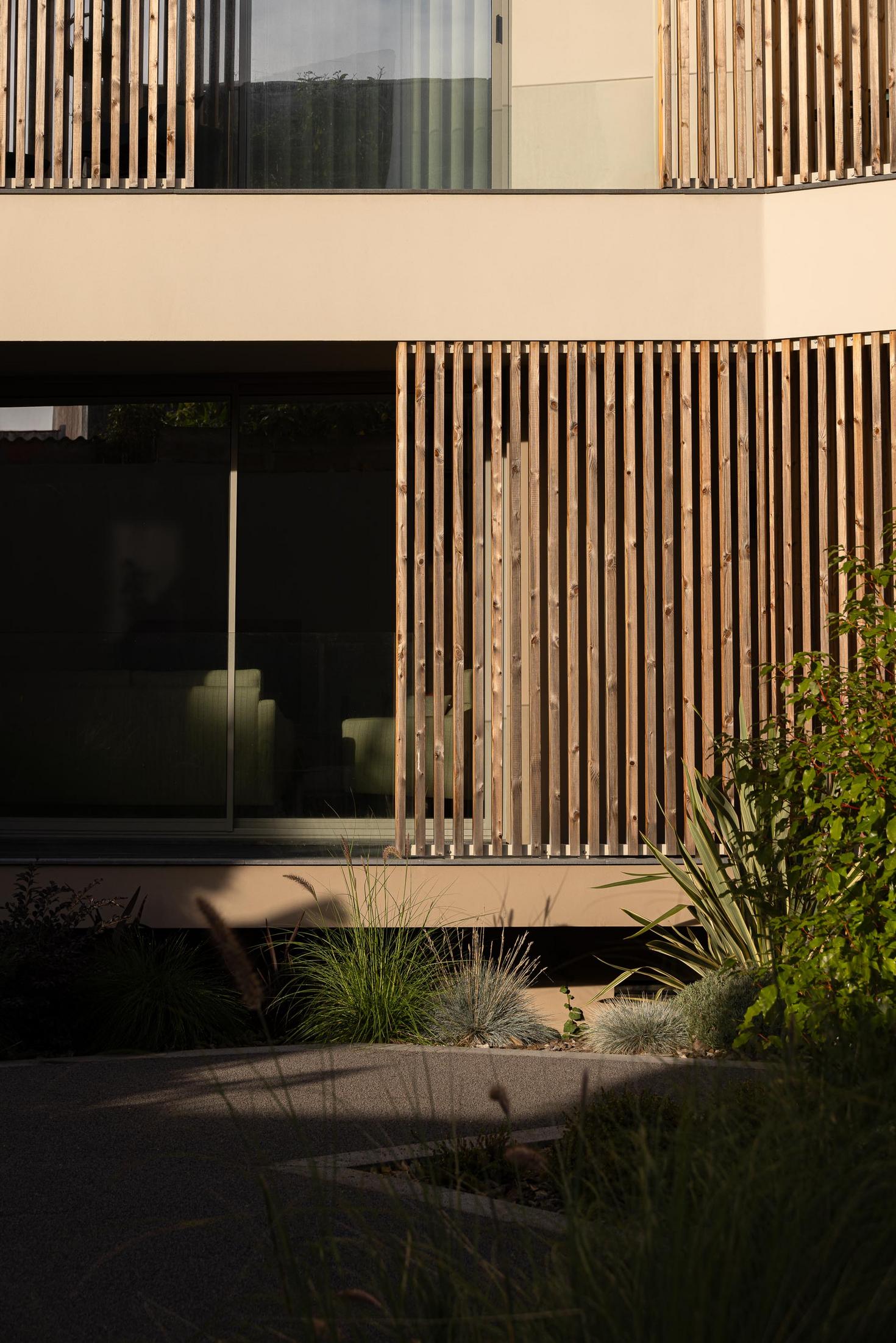 Fachada: Detalhe das ripas de madeira e janela, com vista para o jardim e pavimento em calçada. — ERNESTO DO CANTO - condomínio arquitetura BOX arquitectos em Ponta Delgada