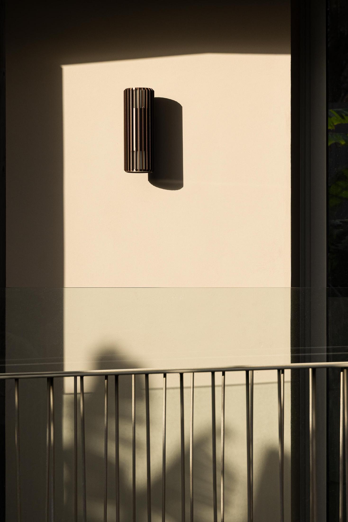 Candeeiro: Detalhe de um candeeiro de parede preto, com ripas verticais, iluminando a fachada bege. — ERNESTO DO CANTO - condomínio arquitetura BOX arquitectos em Ponta Delgada