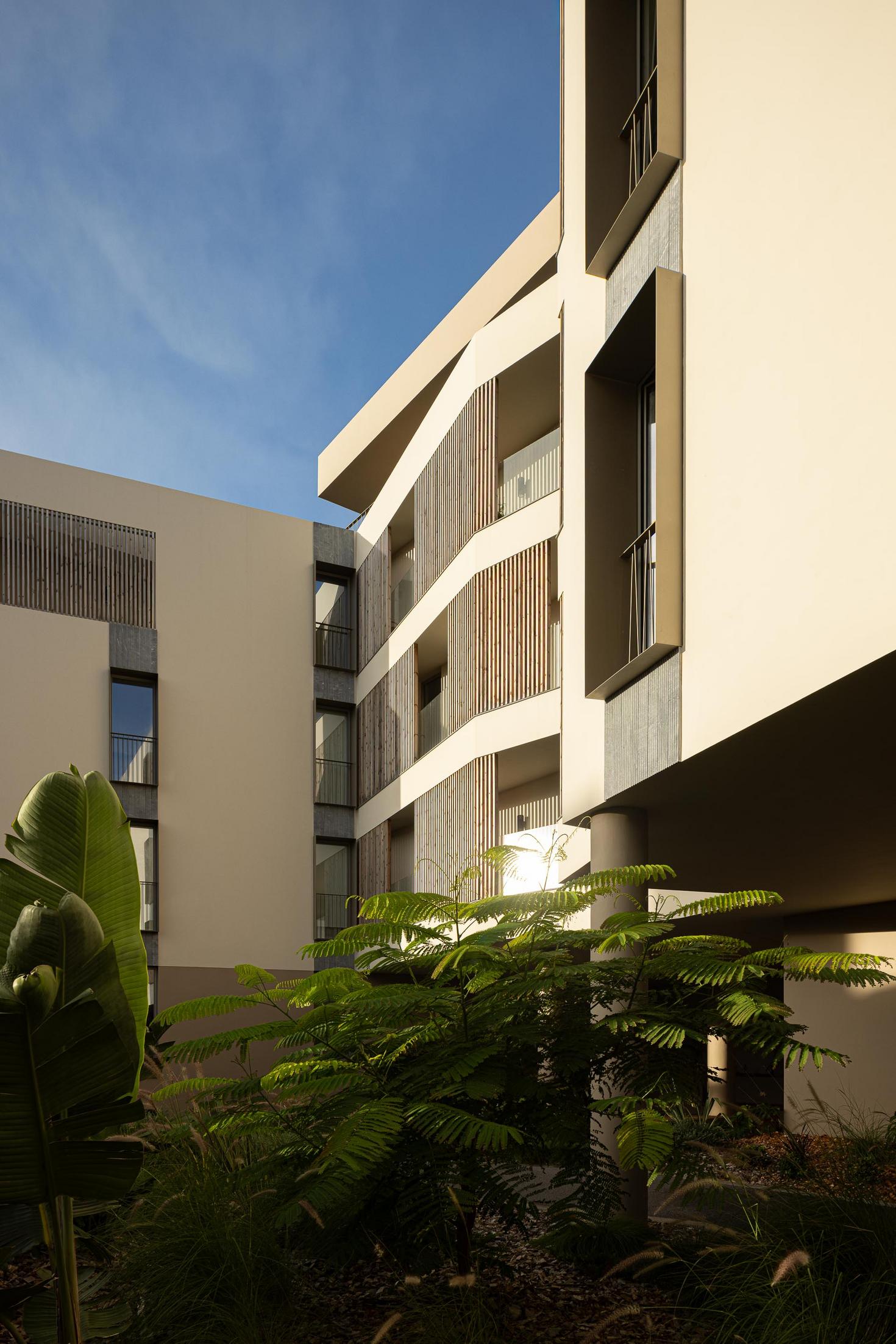 Fachada: Vista do pátio interior com varandas em ripas de madeira e detalhes em pedra. — ERNESTO DO CANTO - condomínio arquitetura BOX arquitectos em Ponta Delgada