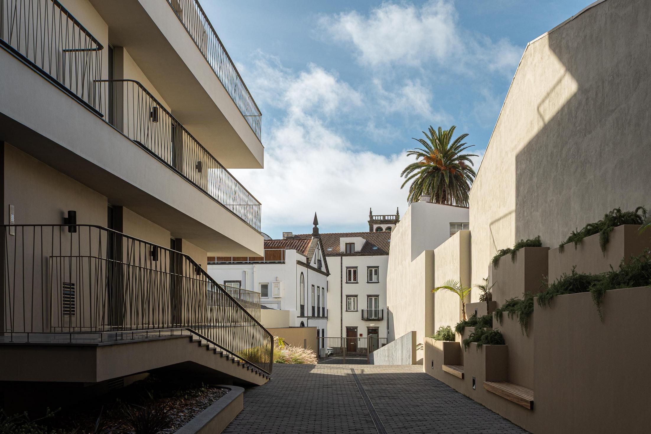 Rua: Edifício moderno contrastando com a arquitetura tradicional, com acesso em calçada. — ERNESTO DO CANTO - condomínio arquitetura BOX arquitectos em Ponta Delgada