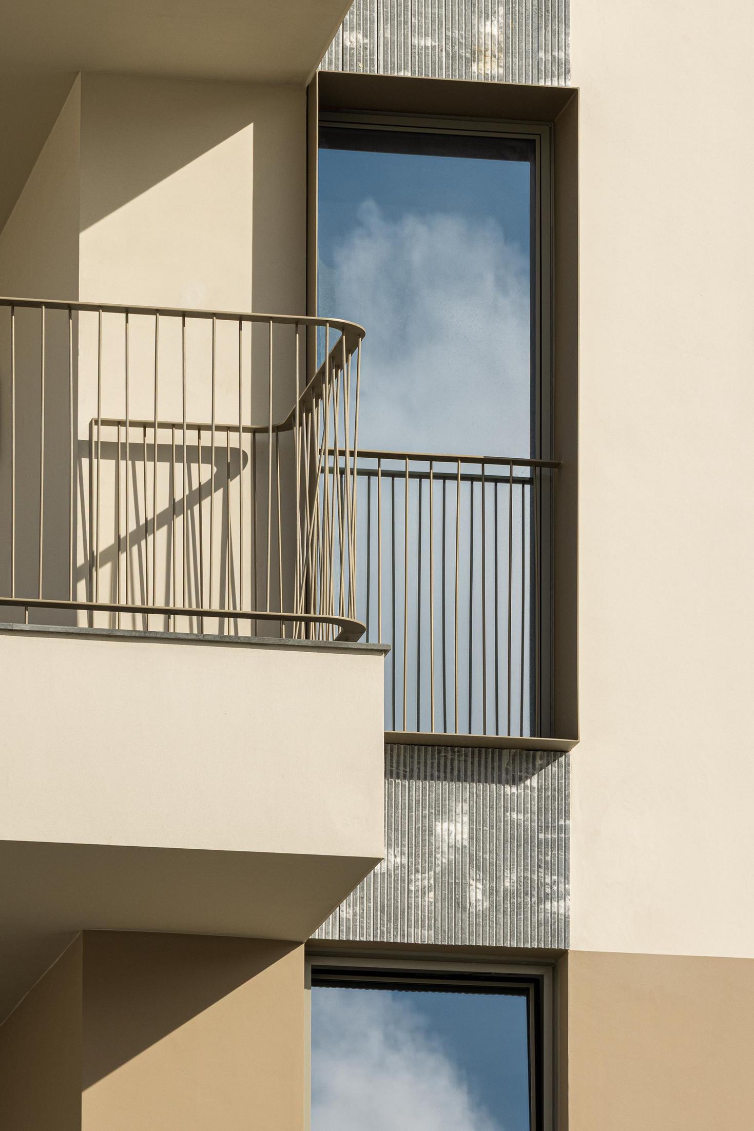 Fachada: Detalhe da varanda com grade metálica dourada e revestimento em pedra. — ERNESTO DO CANTO - condomínio arquitetura BOX arquitectos em Ponta Delgada