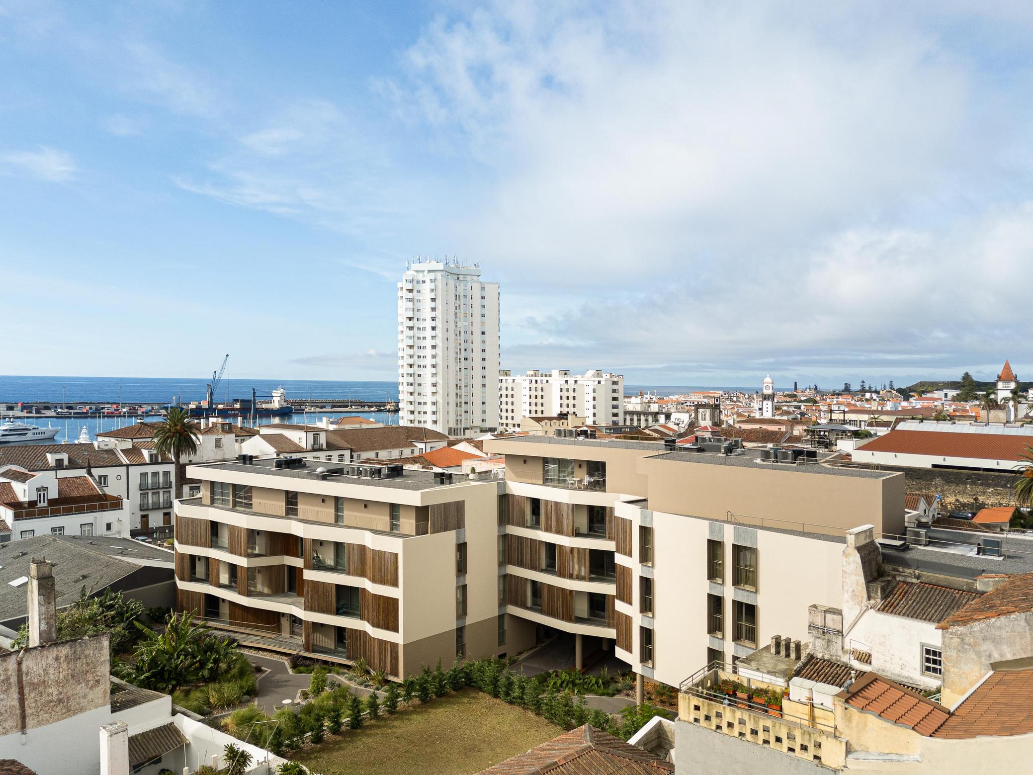 Vista da cidade: Condomínio moderno com detalhes em madeira, integrado na paisagem urbana de Ponta Delgada, com vista para o mar. — ERNESTO DO CANTO - condomínio arquitetura BOX arquitectos em Ponta Delgada