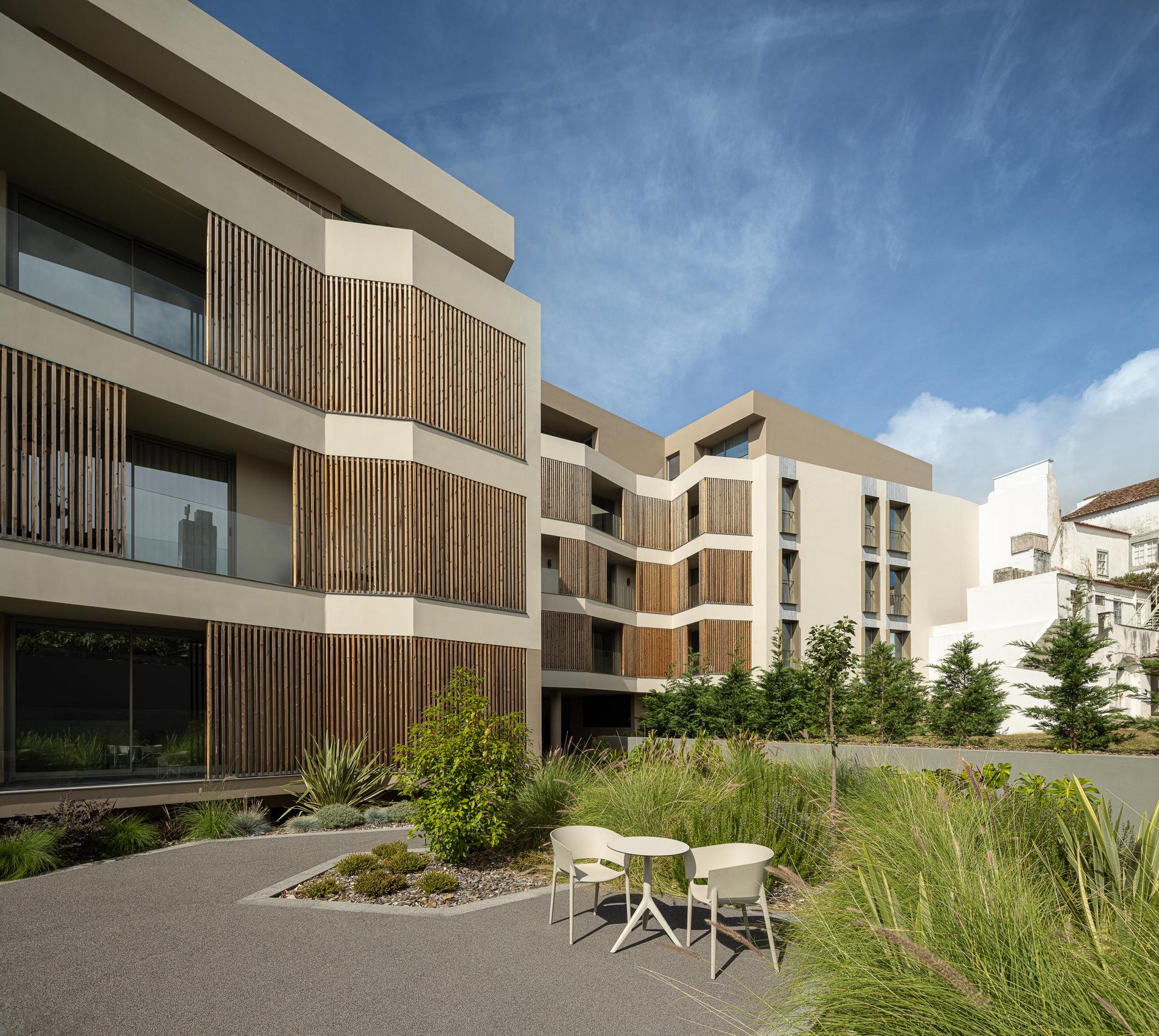 Jardim: Espaço exterior com mesa e cadeiras, pavimento em agregado e vegetação diversa. — ERNESTO DO CANTO - condomínio arquitetura BOX arquitectos em Ponta Delgada