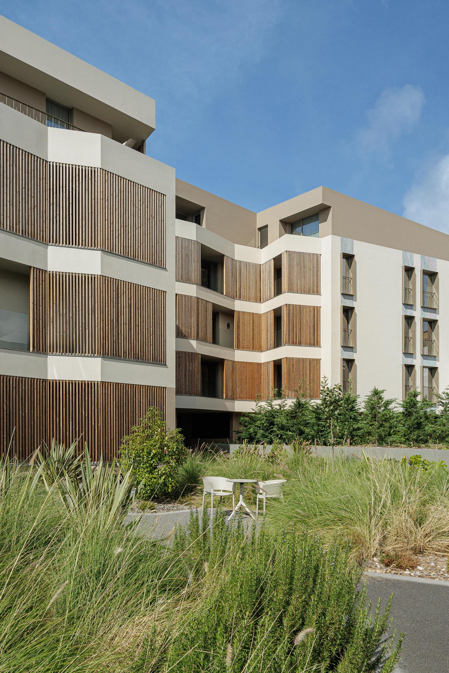 Jardim: Espaço exterior com mesa e cadeiras, pavimento em agregado e vegetação diversa. — ERNESTO DO CANTO - condomínio arquitetura BOX arquitectos em Ponta Delgada