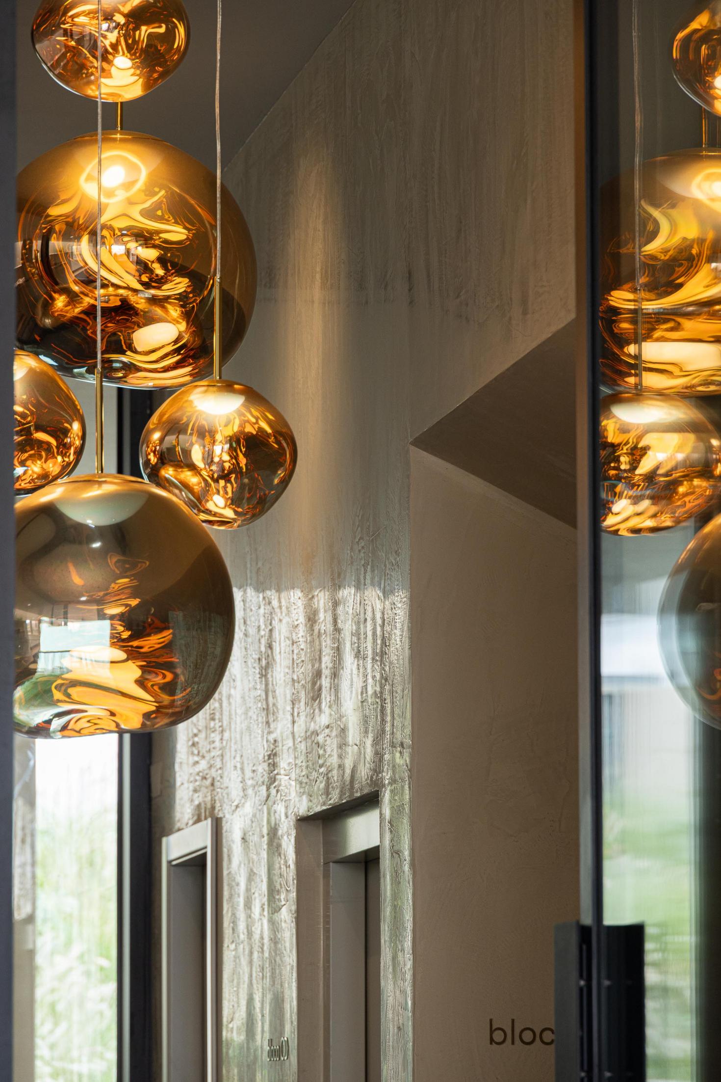 Hall de entrada: Candeeiros suspensos dourados refletindo na parede texturada e elevadores. — ERNESTO DO CANTO - condomínio arquitetura BOX arquitectos em Ponta Delgada