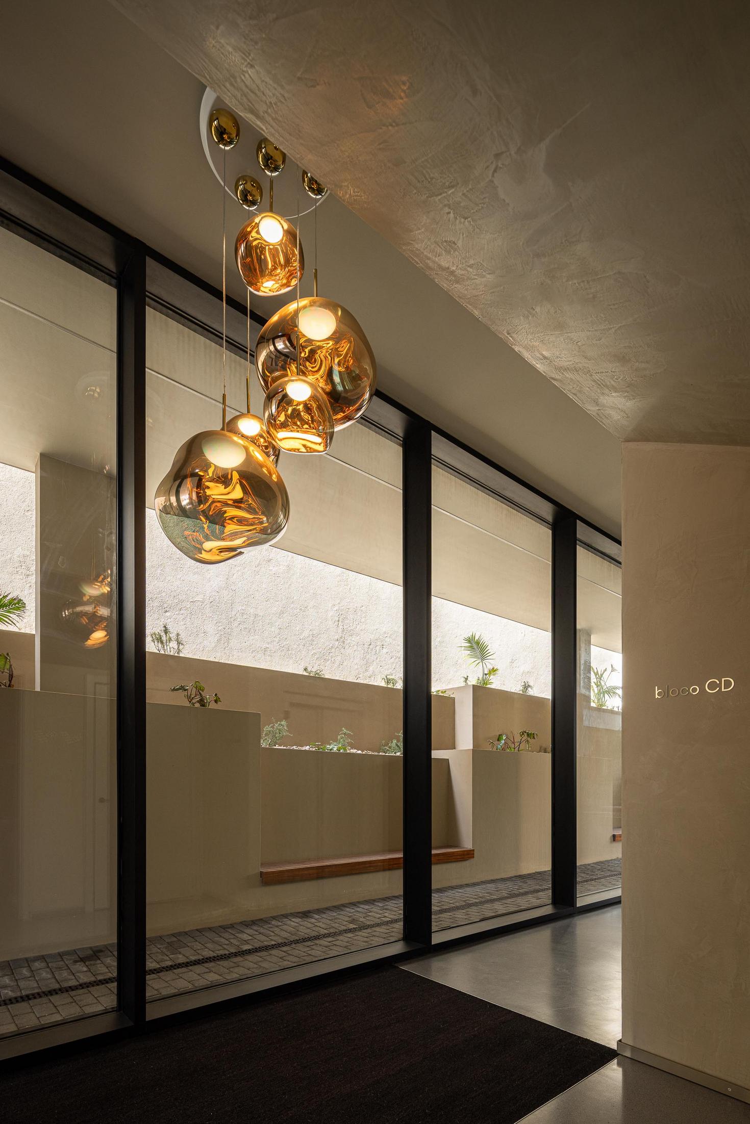 Hall de entrada: Candeeiros suspensos dourados, pavimento em calçada e acesso ao jardim. — ERNESTO DO CANTO - condomínio arquitetura BOX arquitectos em Ponta Delgada