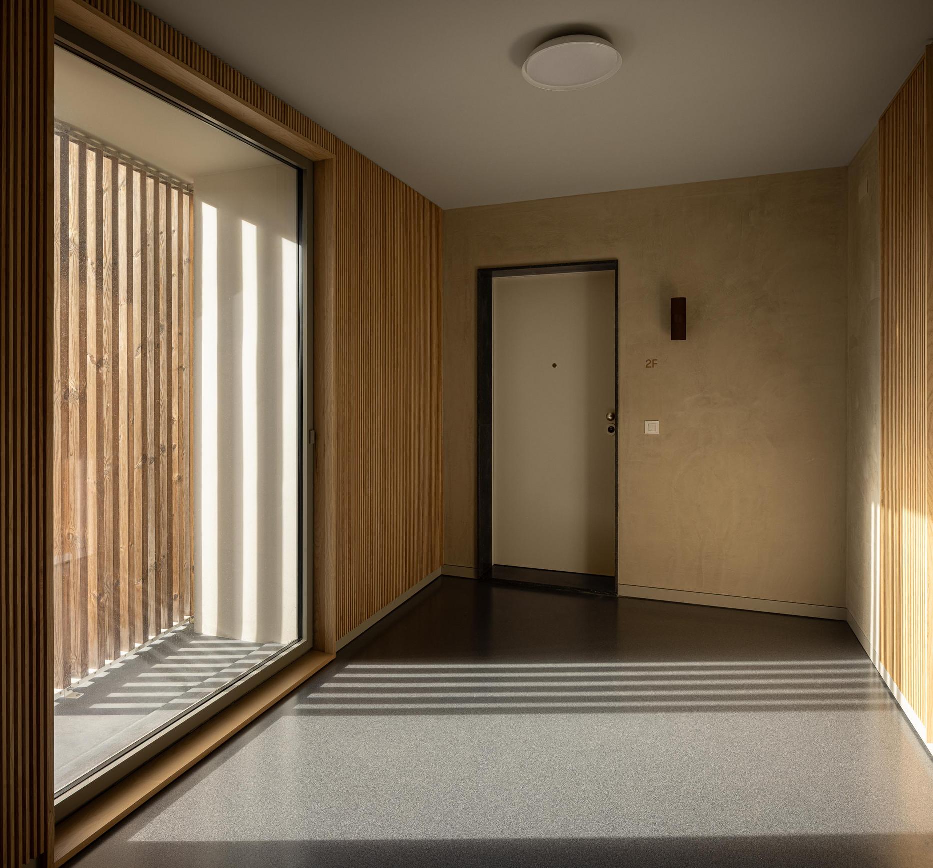 Hall de entrada: Corredor com ripas de madeira nas paredes e pavimento escuro. — ERNESTO DO CANTO - condomínio arquitetura BOX arquitectos em Ponta Delgada