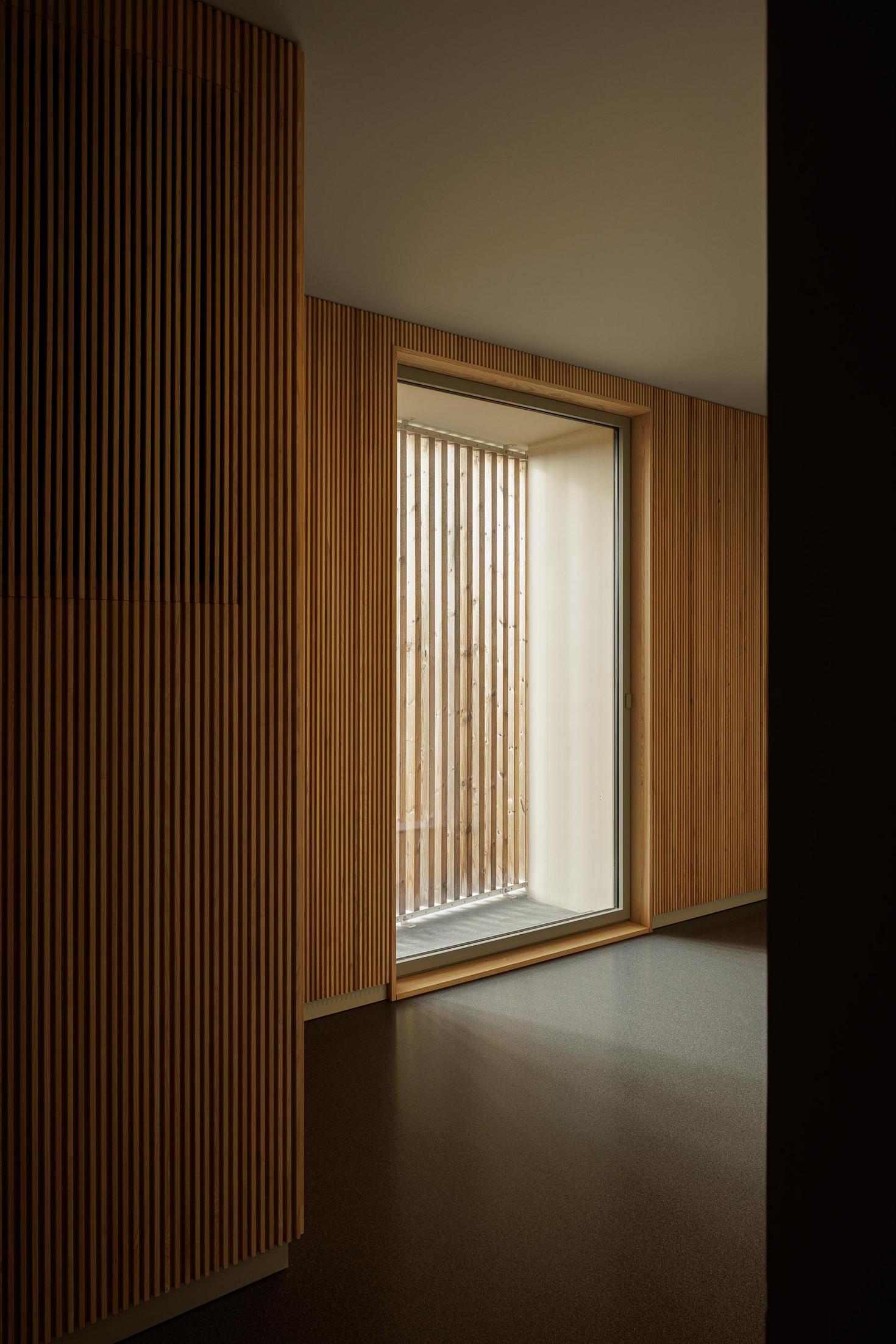 Hall de entrada: Corredor com ripas de madeira nas paredes e pavimento escuro. — ERNESTO DO CANTO - condomínio arquitetura BOX arquitectos em Ponta Delgada