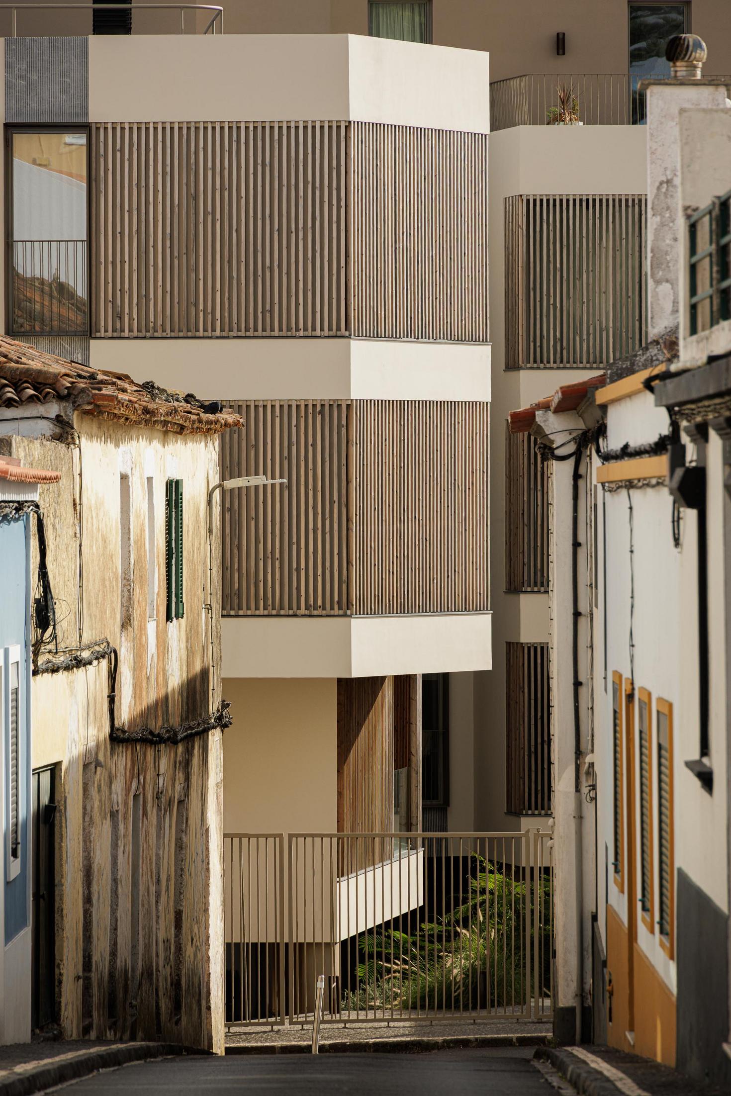 Rua: Edifício moderno contrastando com a arquitetura tradicional, visto de uma rua estreita. — ERNESTO DO CANTO - condomínio arquitetura BOX arquitectos em Ponta Delgada