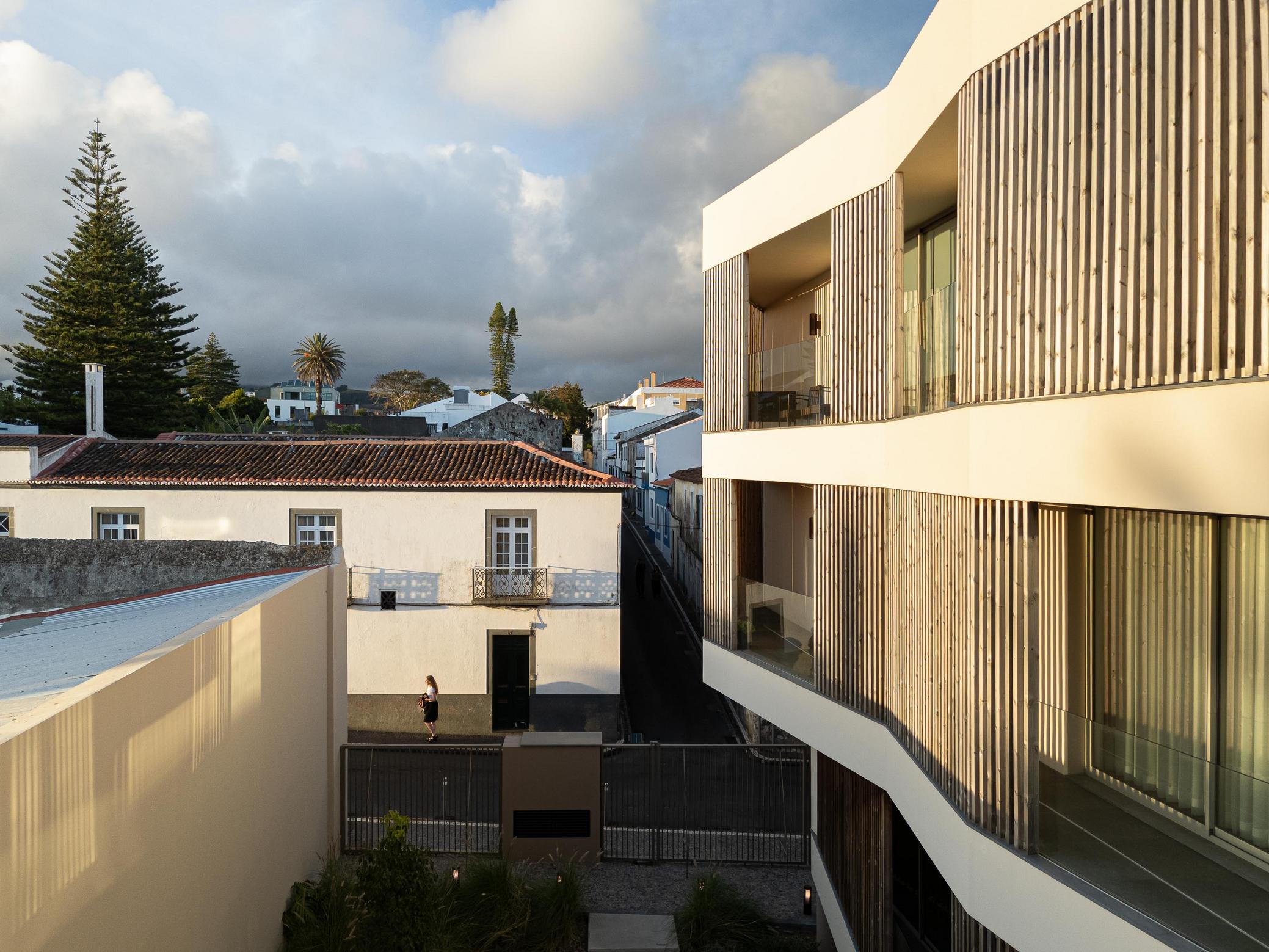 Vista da cidade: Edifício moderno integrado na paisagem urbana, com casas tradicionais. — ERNESTO DO CANTO - condomínio arquitetura BOX arquitectos em Ponta Delgada