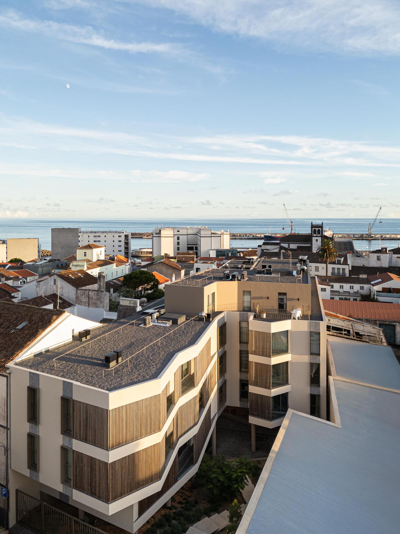 Vista da cidade: Edifício moderno integrado na paisagem urbana, com vista para o mar. — ERNESTO DO CANTO - condomínio arquitetura BOX arquitectos em Ponta Delgada