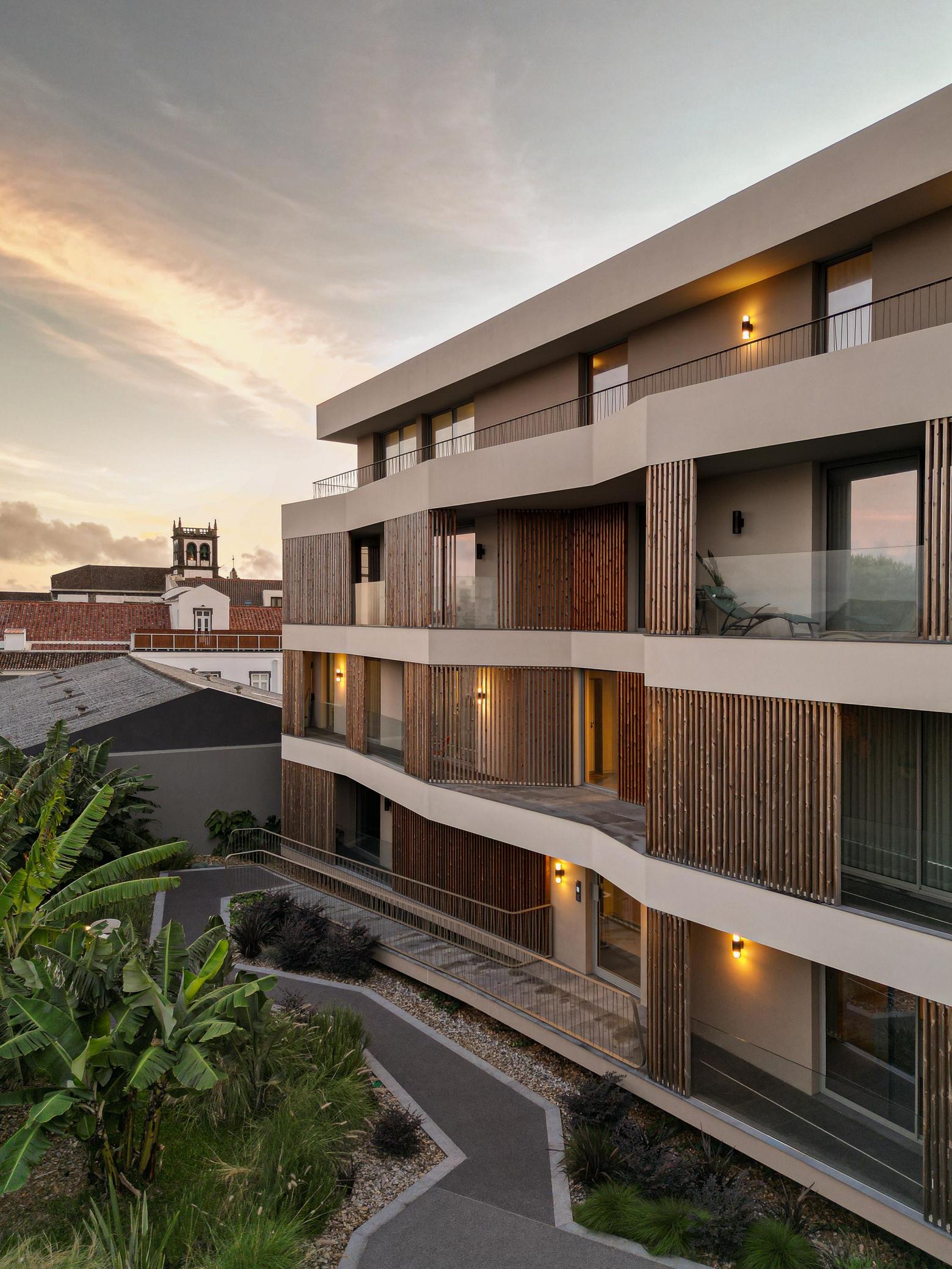 Fachada: Vista do edifício com varandas em ripas de madeira e rampa de acesso. — ERNESTO DO CANTO - condomínio arquitetura BOX arquitectos em Ponta Delgada