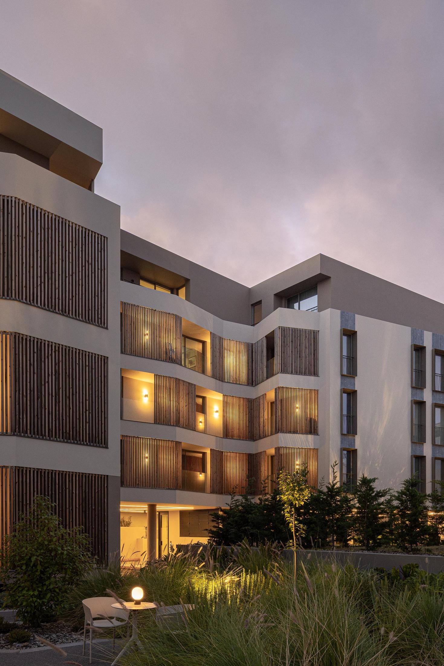 Fachada: Vista do edifício com varandas em ripas de madeira e iluminação noturna. — ERNESTO DO CANTO - condomínio arquitetura BOX arquitectos em Ponta Delgada