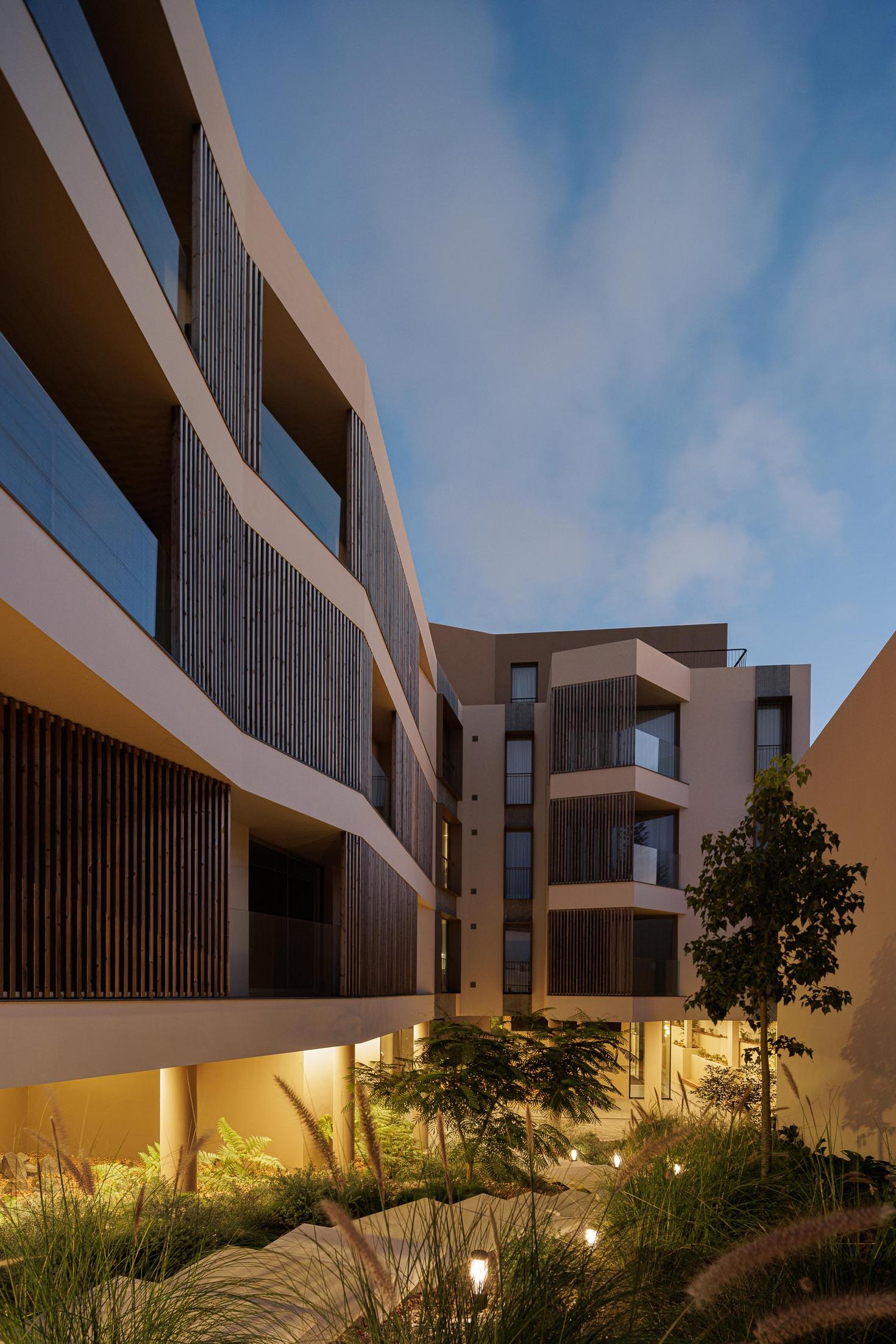 Fachada: Detalhe das varandas com ripas de madeira e iluminação noturna. — ERNESTO DO CANTO - condomínio arquitetura BOX arquitectos em Ponta Delgada