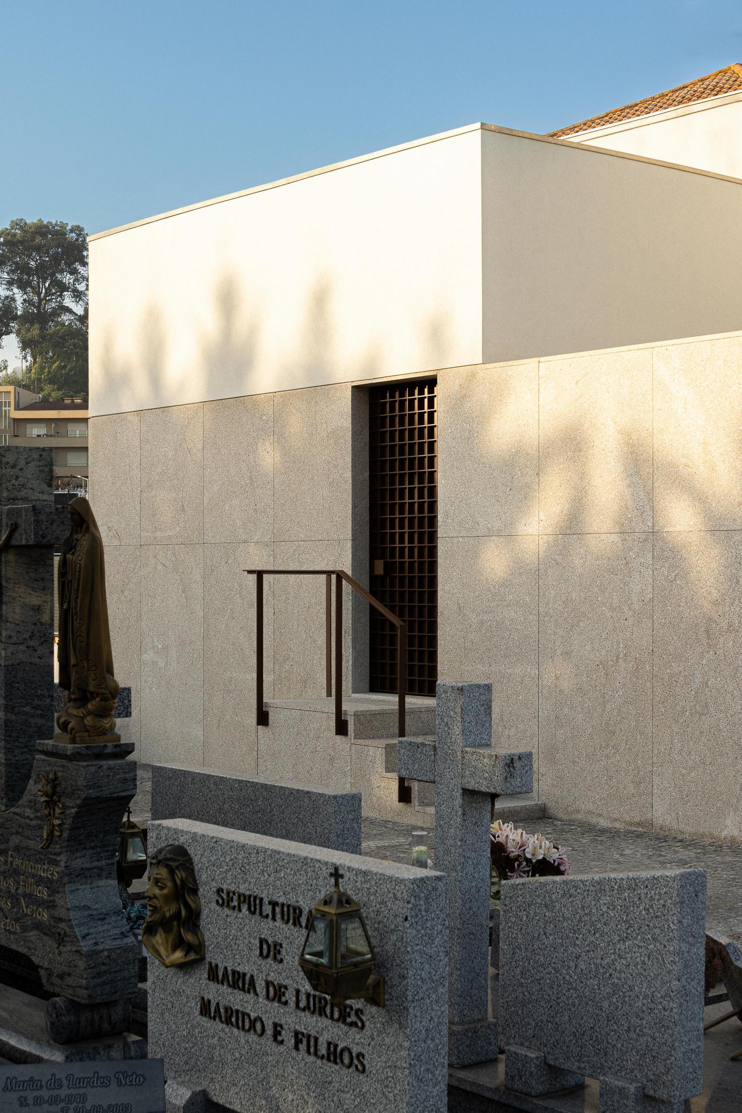 Entrada: Fachada em granito com porta gradeada, integrada no cemitério. Estilo minimalista. — Casa Mortuária São Martinho do Campo arquitetura Multiprojectus em Santo Tirso