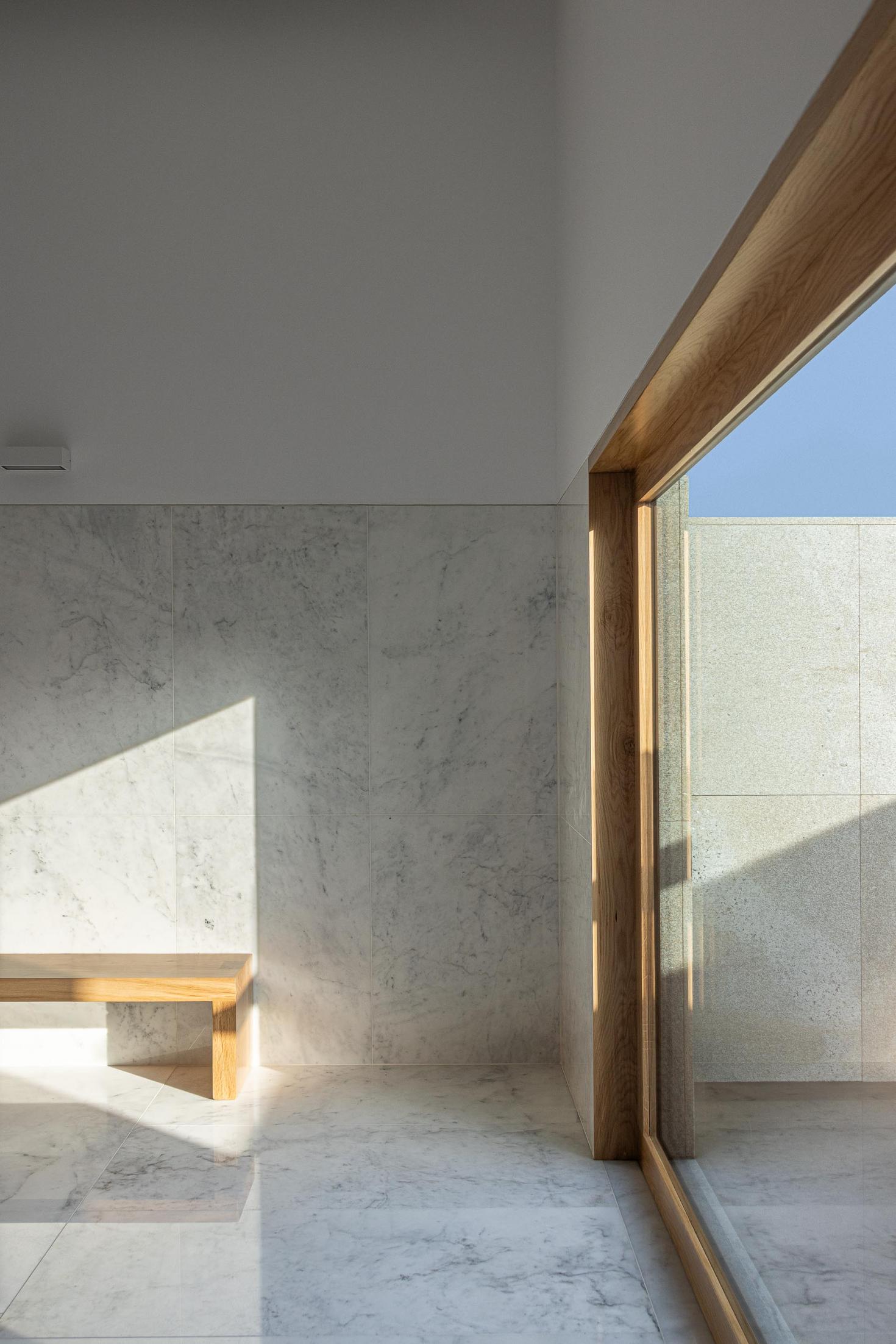 Capela: Detalhe da janela com caixilharia de madeira e parede em mármore. — Casa Mortuária São Martinho do Campo arquitetura Multiprojectus em Santo Tirso