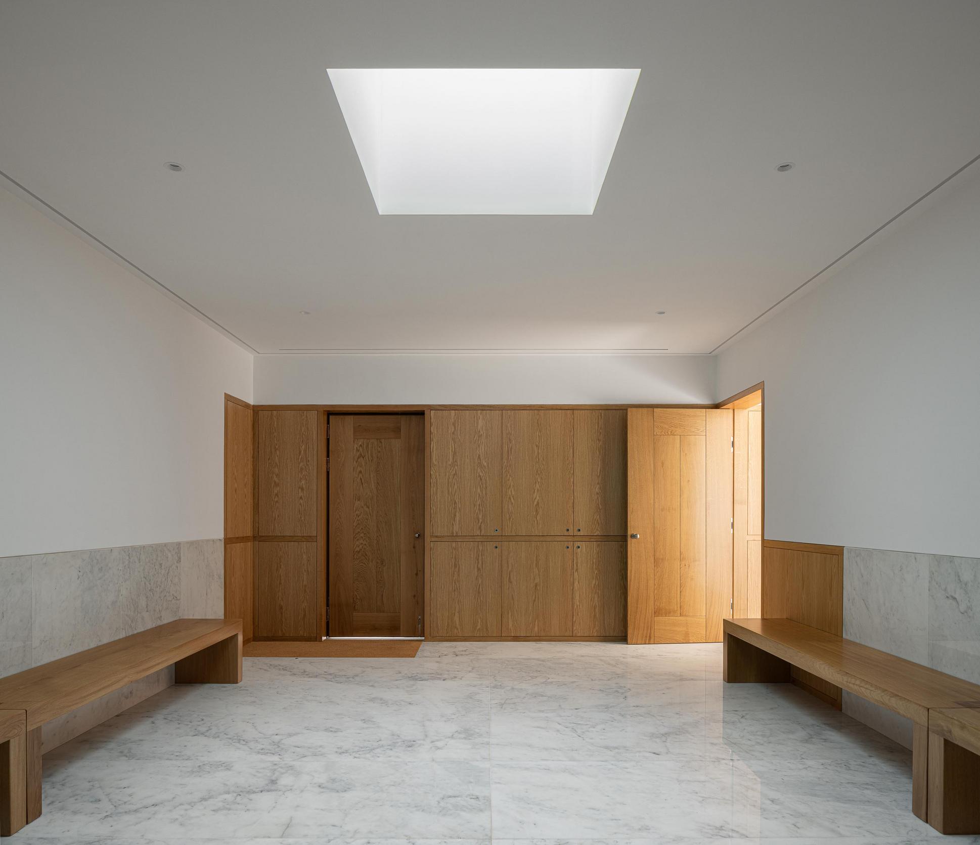 Hall de entrada: Pavimento em mármore, paredes brancas e lambrim de madeira com bancos. — Casa Mortuária São Martinho do Campo arquitetura Multiprojectus em Santo Tirso