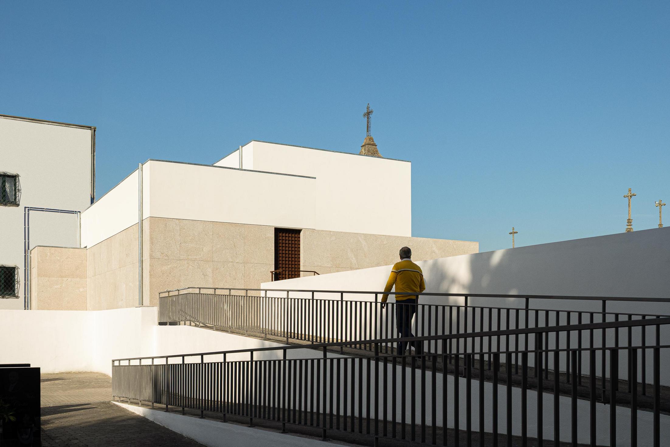 Exterior: Rampa de acesso à casa mortuária, com corrimão metálico e fachada minimalista. — Casa Mortuária São Martinho do Campo arquitetura Multiprojectus em Santo Tirso