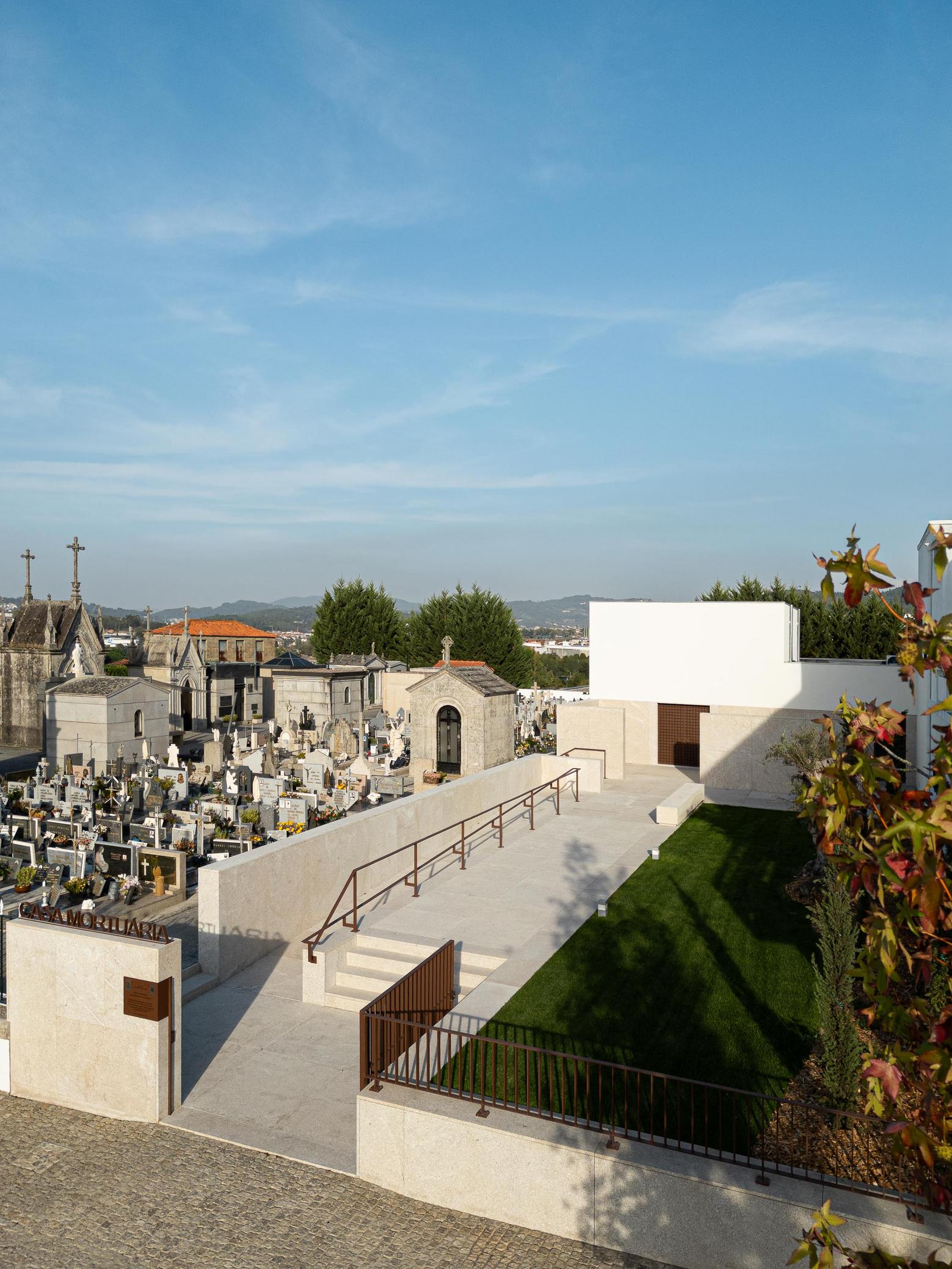 Exterior: Acesso à casa mortuária com rampa, jardim relvado e cemitério em redor. — Casa Mortuária São Martinho do Campo arquitetura Multiprojectus em Santo Tirso