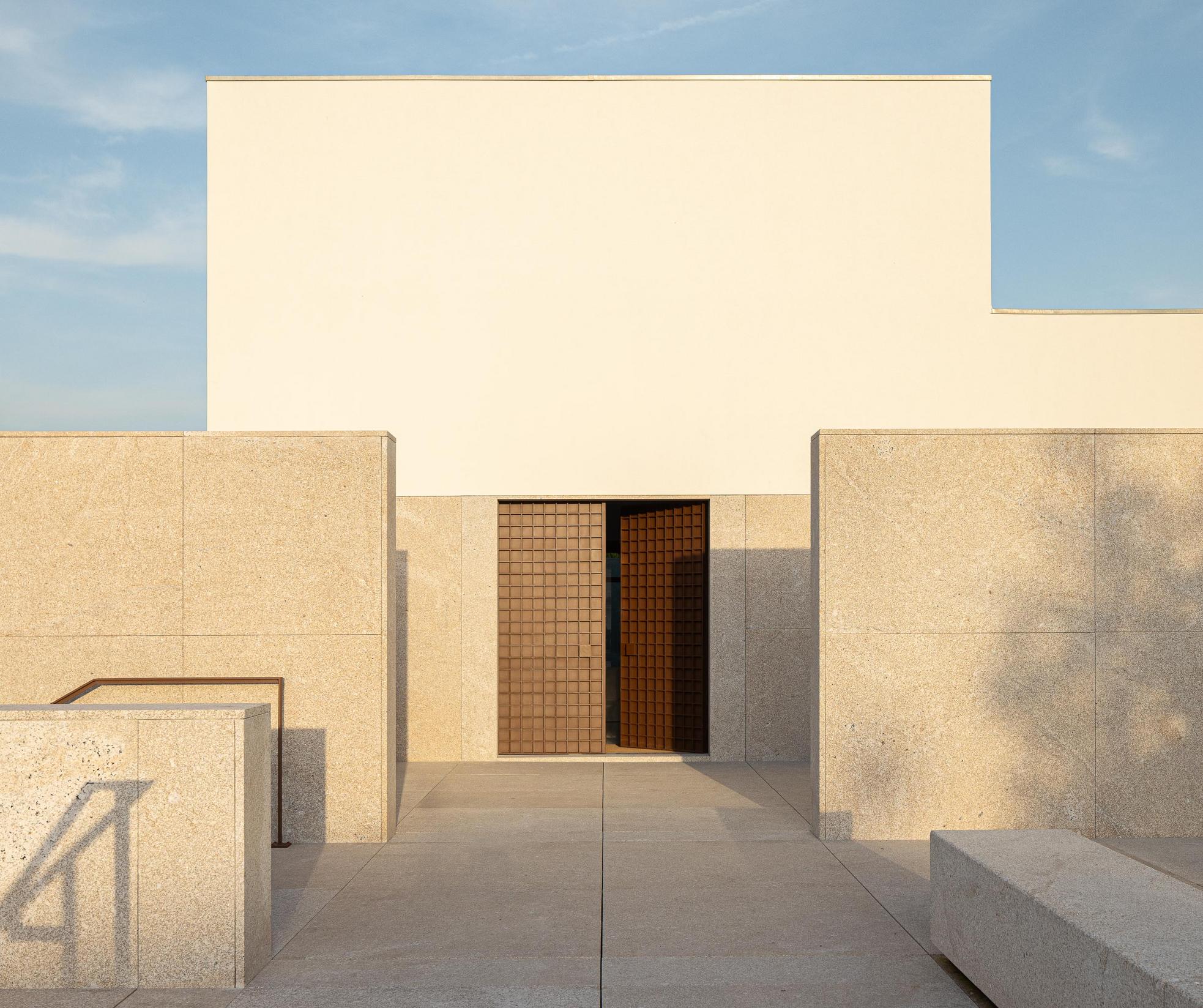 Exterior: Entrada principal da casa mortuária, com paredes em granito e porta gradeada. — Casa Mortuária São Martinho do Campo arquitetura Multiprojectus em Santo Tirso