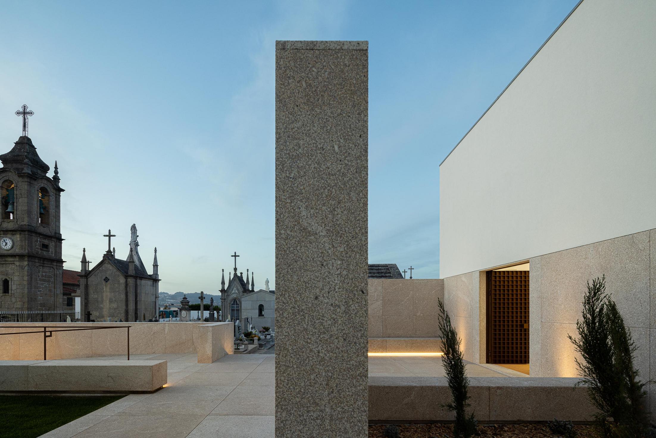 Exterior: Casa mortuária e torre da igreja, com iluminação noturna e pátio ajardinado. — Casa Mortuária São Martinho do Campo arquitetura Multiprojectus em Santo Tirso