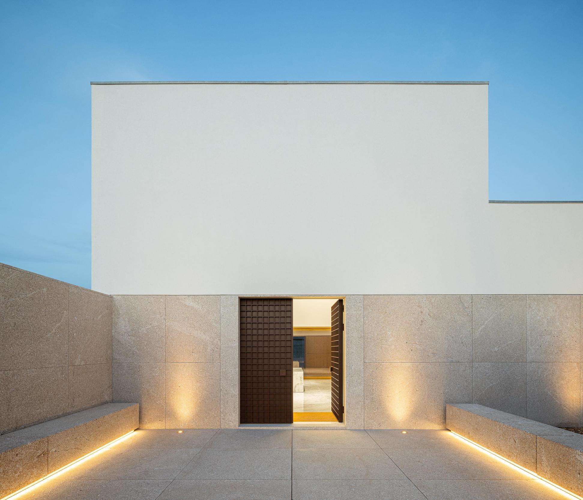 Exterior: Entrada iluminada da casa mortuária, com bancos de granito e iluminação embutida. — Casa Mortuária São Martinho do Campo arquitetura Multiprojectus em Santo Tirso