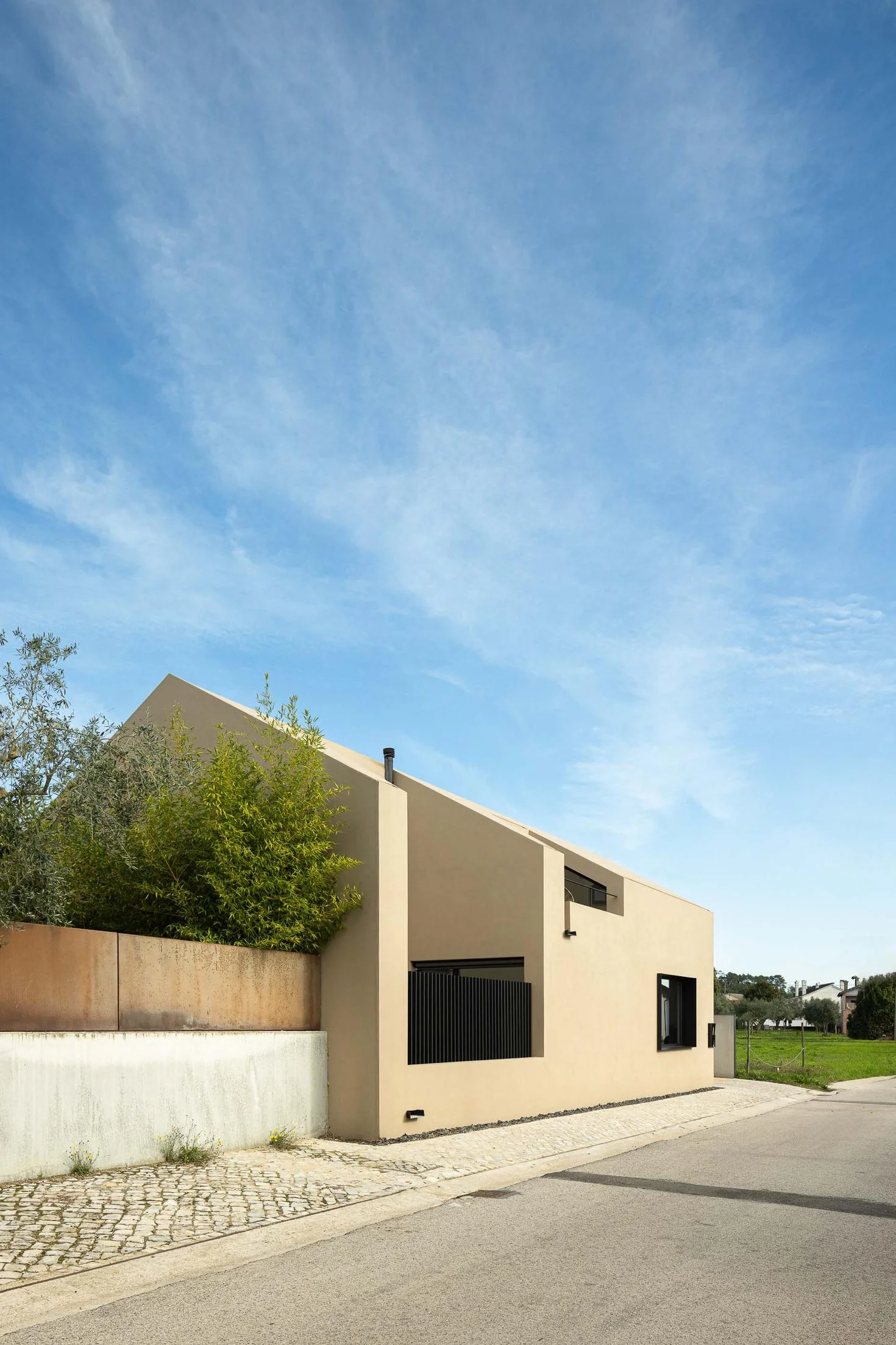 Exterior: Casa bege com telhado inclinado, janela preta e passeio em calçada portuguesa. — CASINHA DA MELROEIRA arquitetura Filipe Saraiva Arquitectos em Ourém